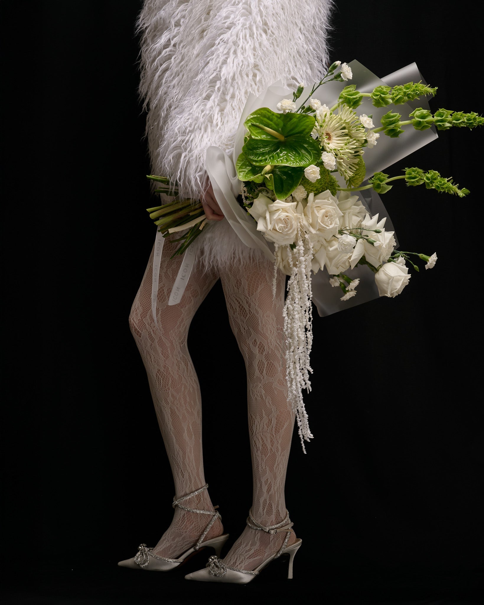 Legs in white tights, fur coat and fashionable shoes holding a white and green bouquet from Flower Icon
