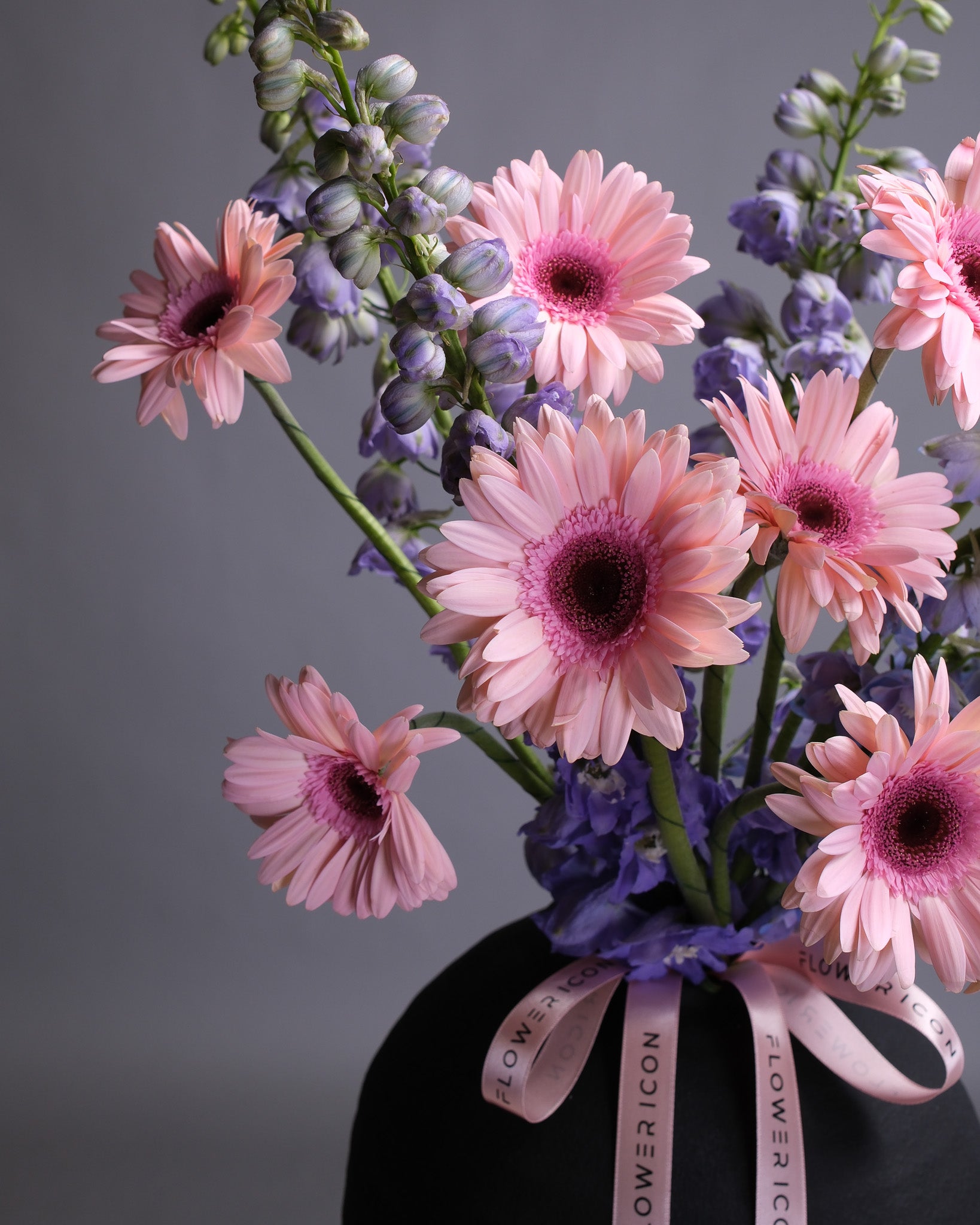 Bouquet of pink and purple flowers with a black vase on a gray background
