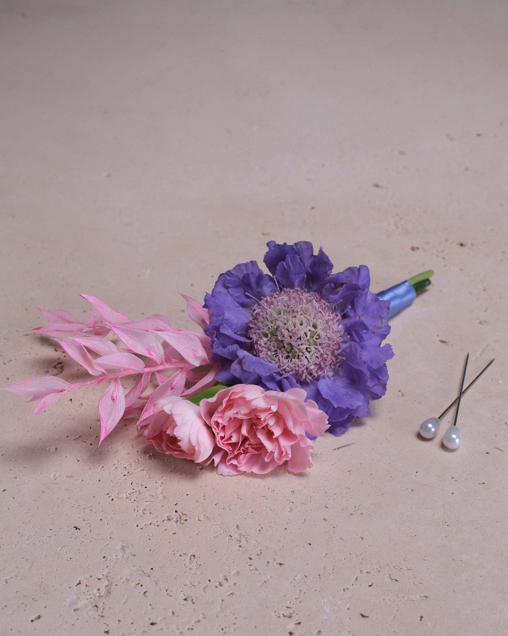 Boutonniere Floral arrangement with pink and purple flowers on a beige surface