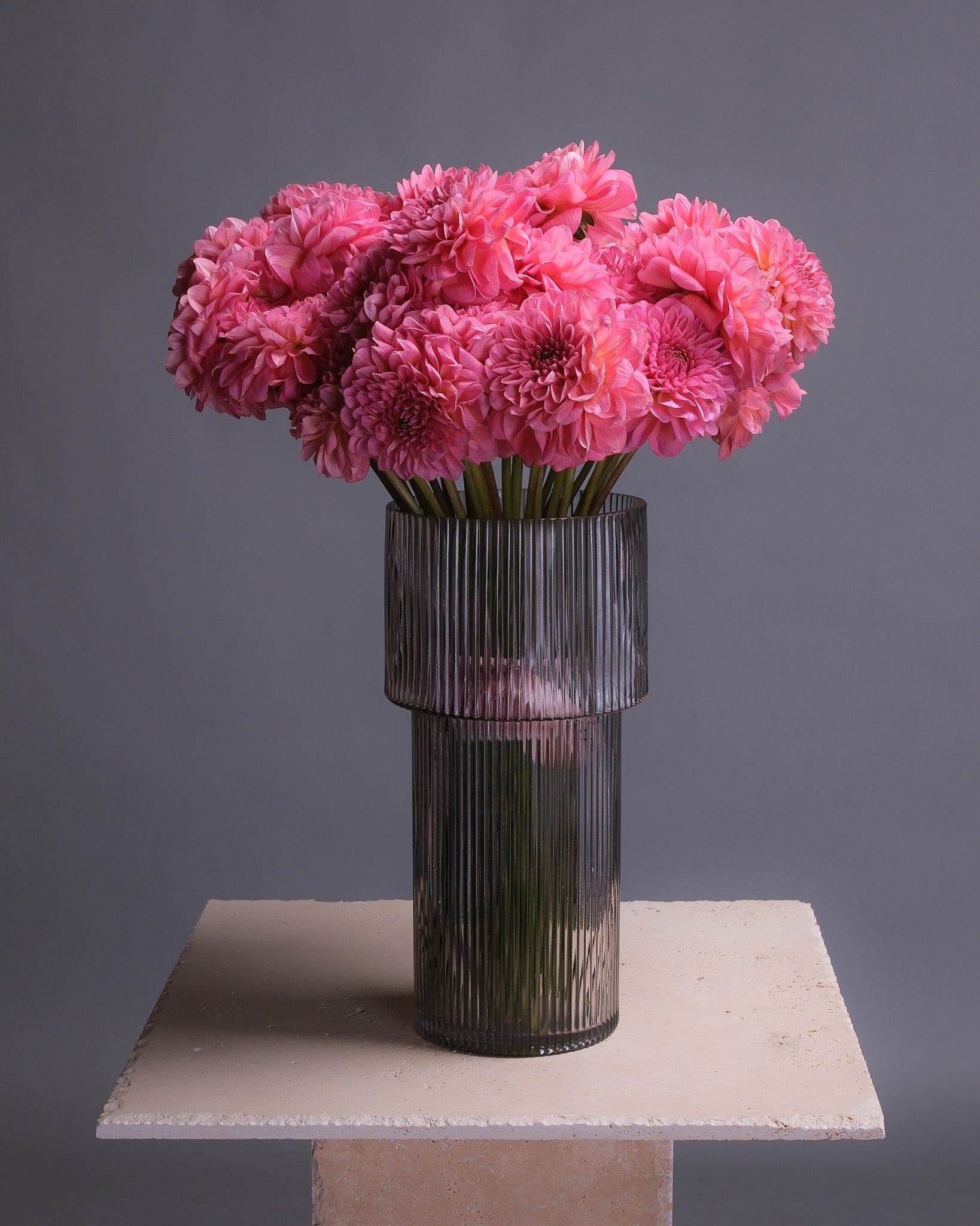 Dahlia bouquet arranged in a modern glass vase, featuring pink and orange dahlias with greenery, styled for interior display.