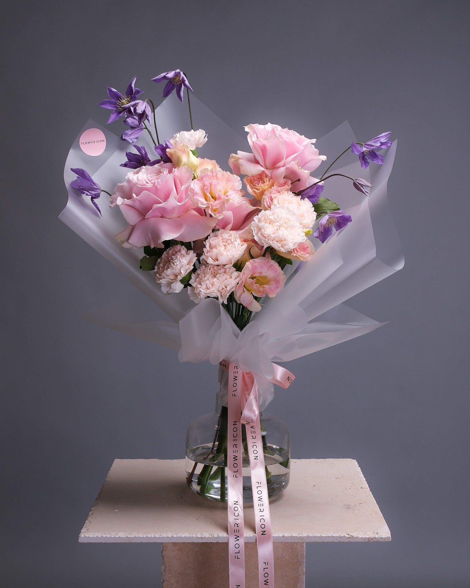 Elegant bouquet in a vase featuring pink roses, purple clematis, blush carnations, and blush lisianthus in a soft, romantic palette.