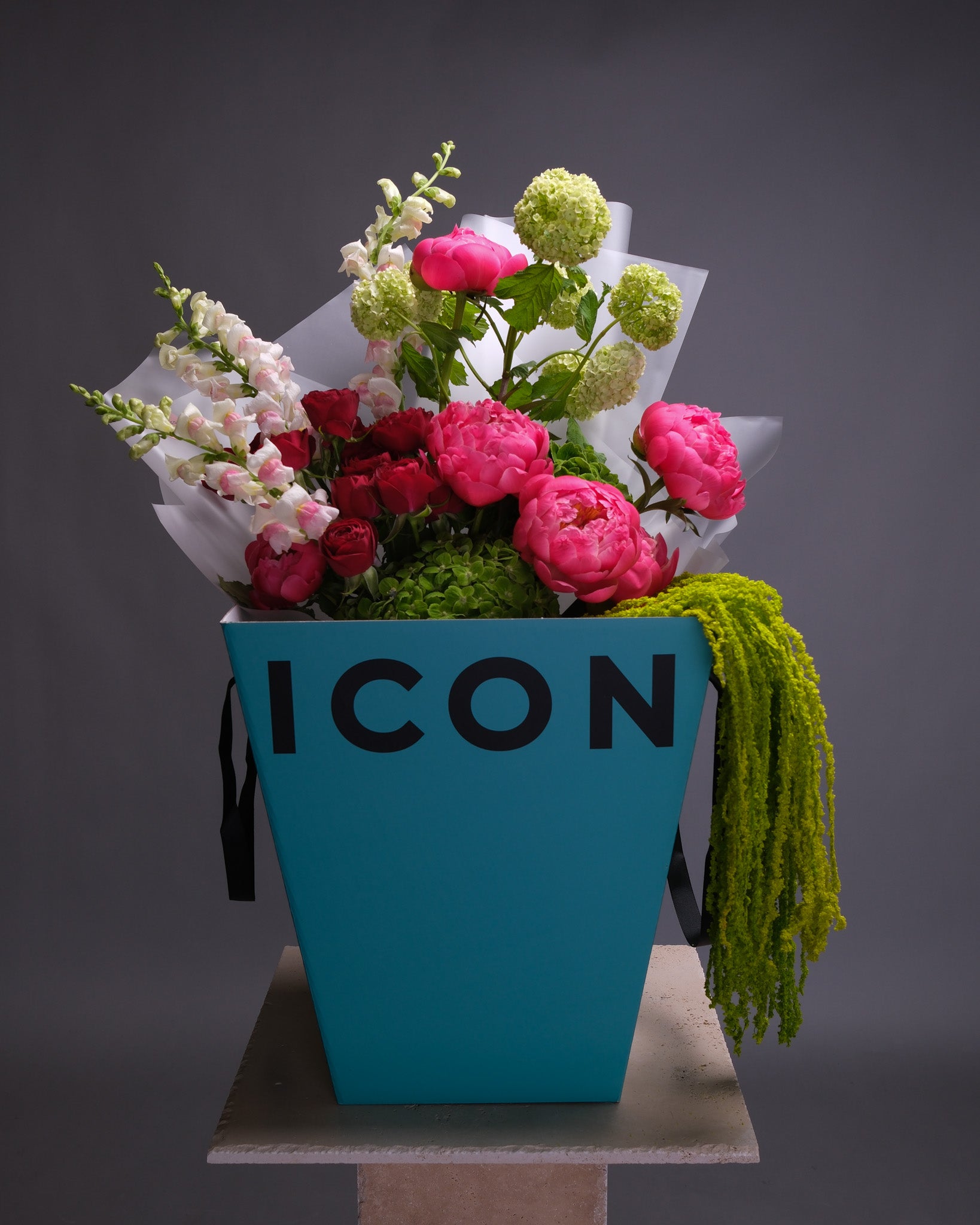Luxurious bouquet arranged in a signature box, showcasing green hydrangeas, coral peonies, red roses, and textured greenery.