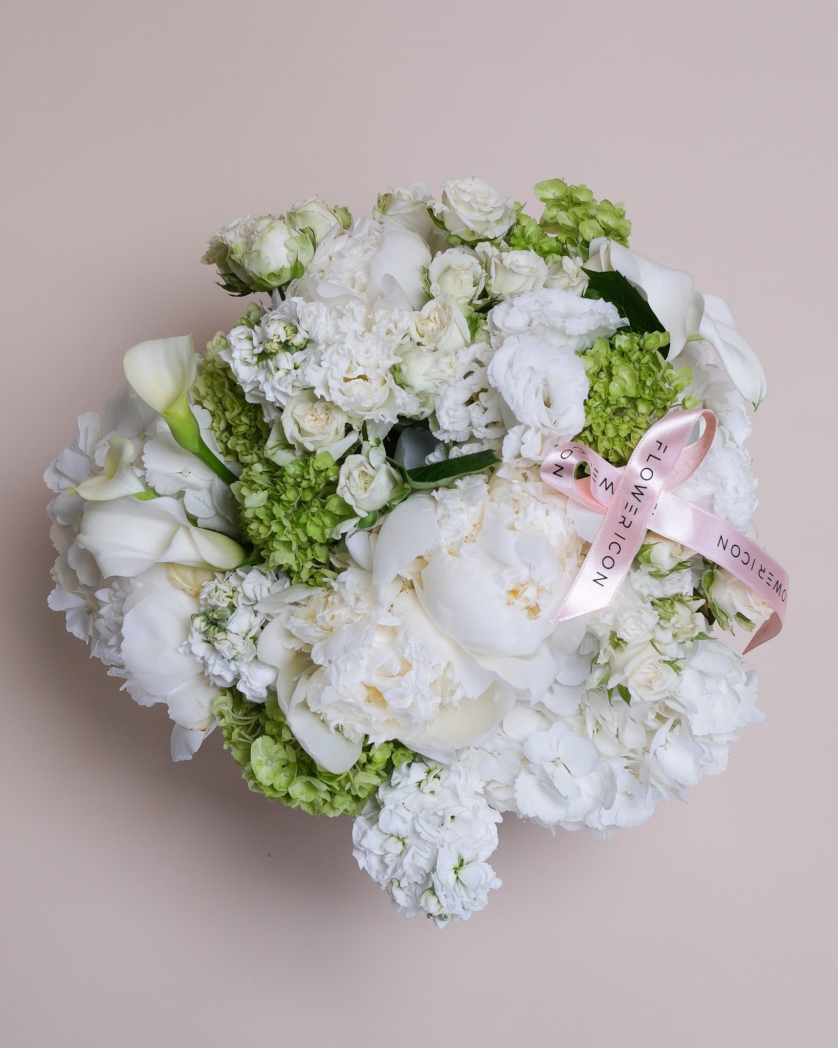 Top view of a luxurious white bouquet arranged in a vase, featuring white peonies, hydrangeas, and elegant calla lilies in a full, rounded design.