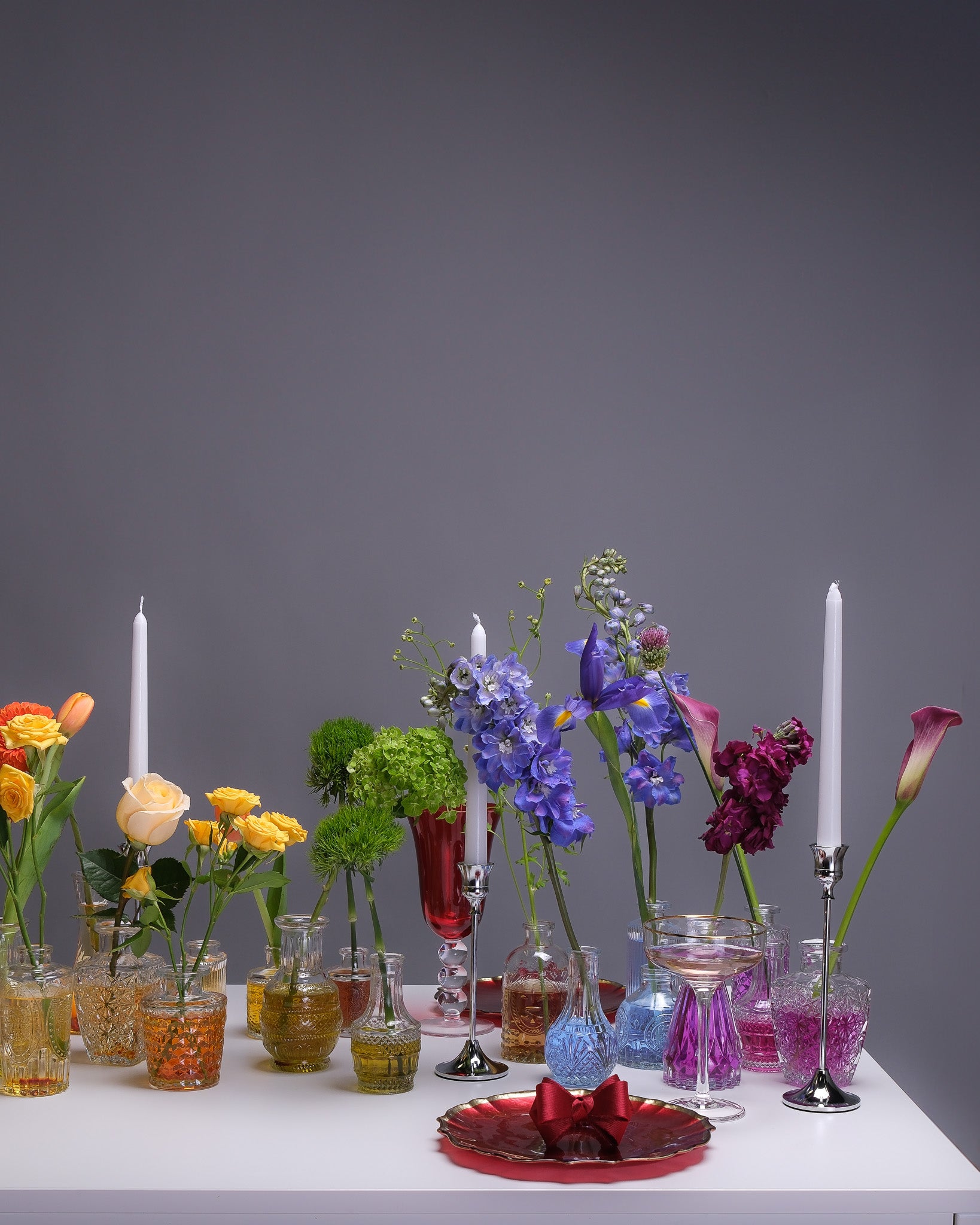Close-up of a rainbow floral centerpiece featuring roses, tulips, delphinium, and hydrangeas in vivid, saturated hues.