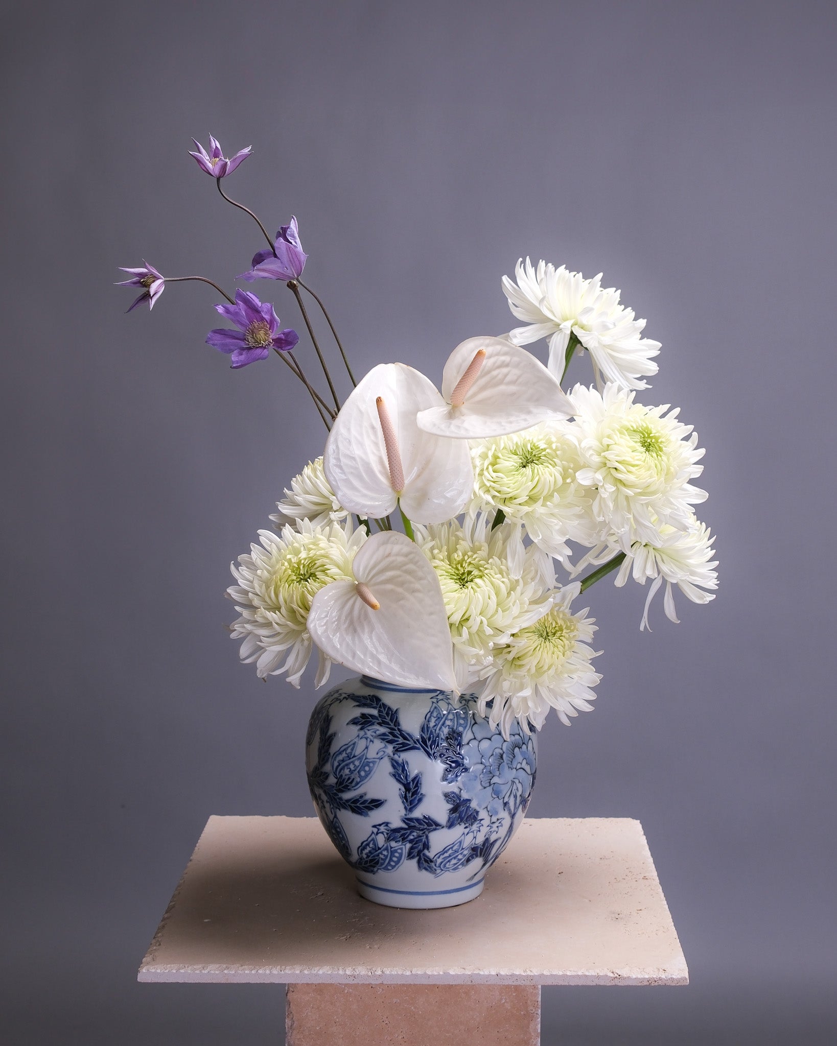 Elegant Asian-inspired floral arrangement featuring white chrysanthemums, sculptural white anthurium, and trailing purple clematis in a minimalist, balanced design.