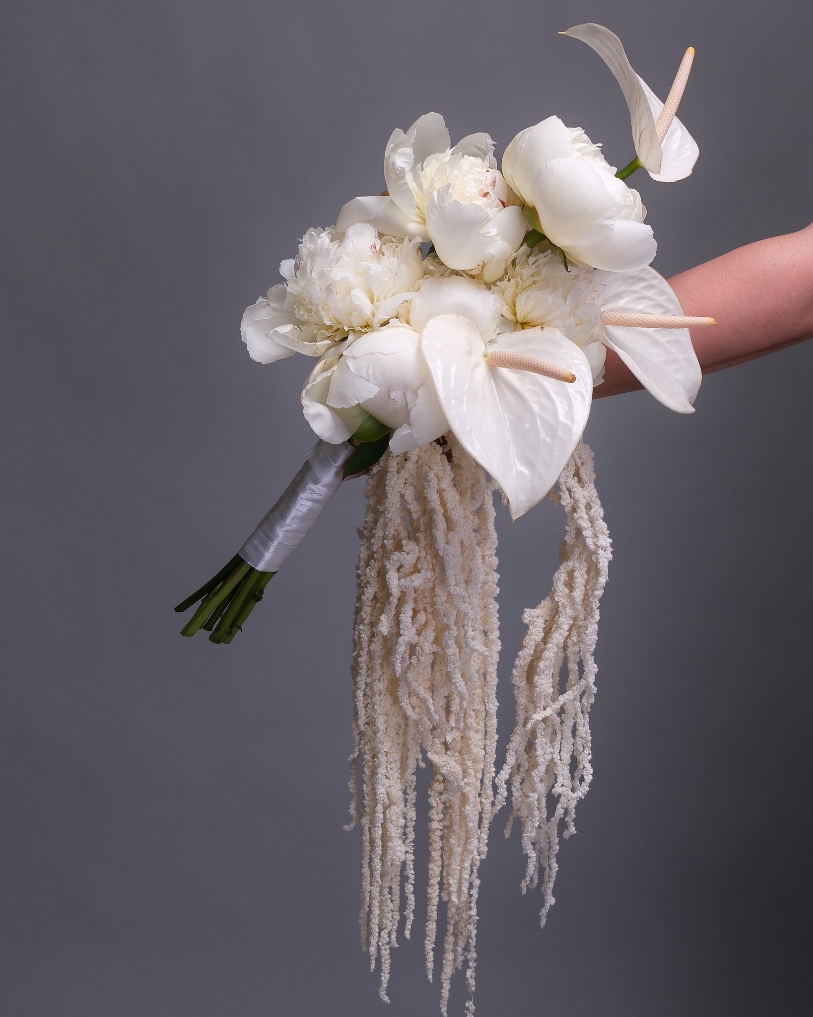 Side angle of a contemporary white bridal bouquet with bold white anthurium and soft peonies, showcasing its clean lines and elegant form.