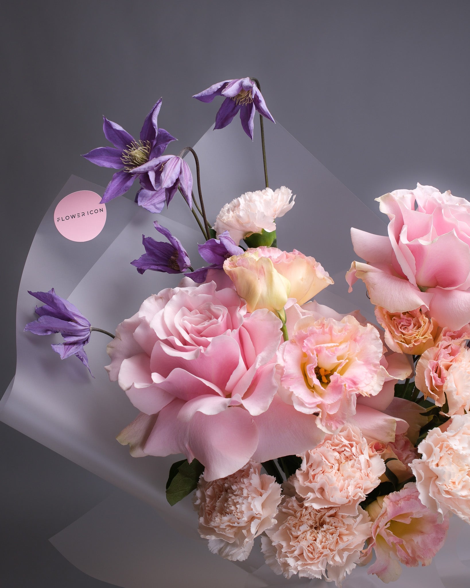 Close-up of delicate pink roses, blush lisianthus, carnations, and purple clematis, highlighting soft textures and pastel hues.