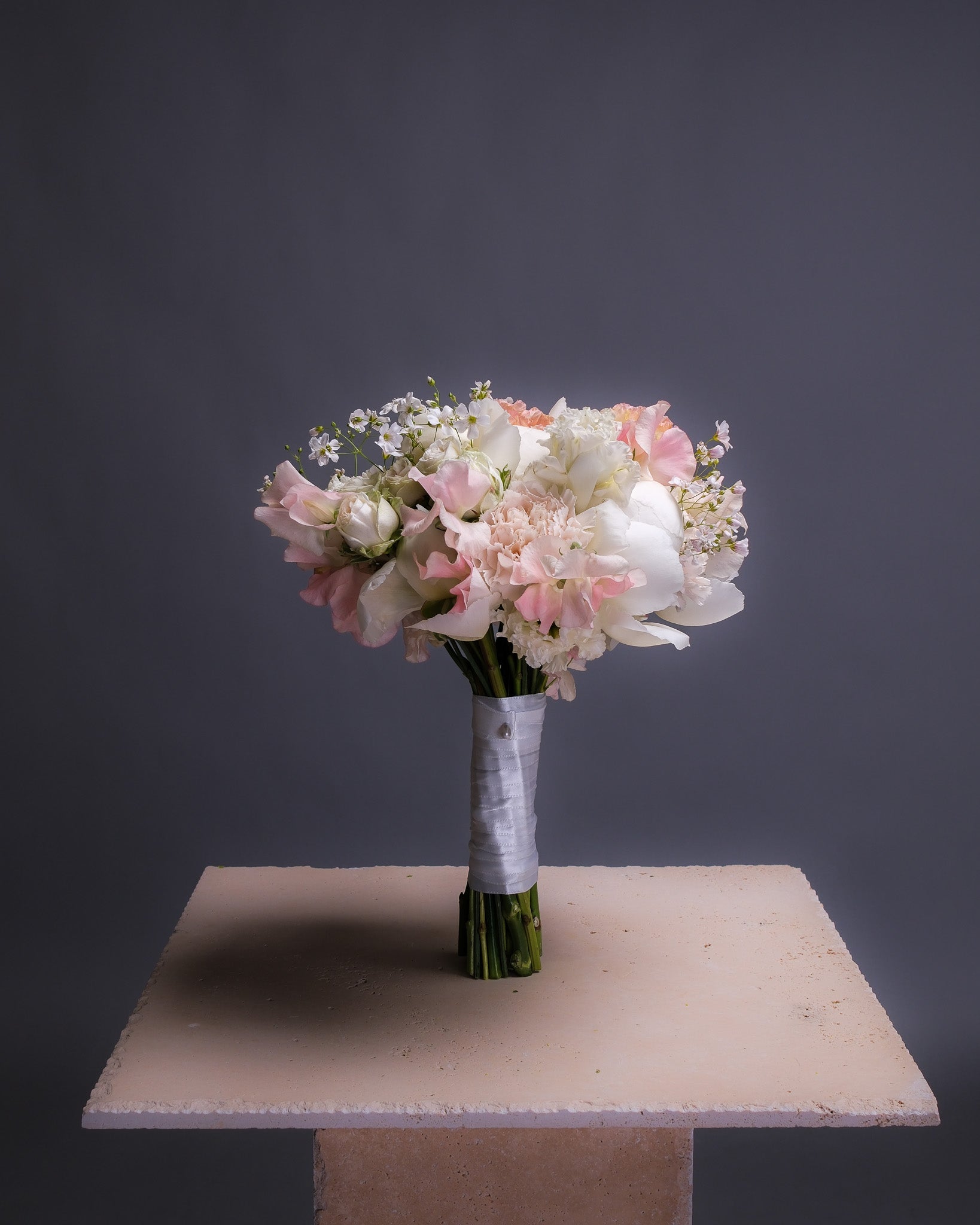 Romantic bridal bouquet in soft blush and white tones, featuring white peonies, lisianthus, and sweet peas, arranged in a classic round shape with a delicate, airy feel.