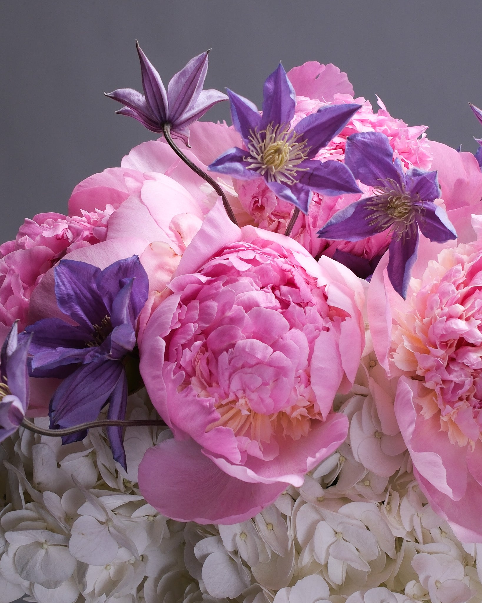 Close-up of a romantic bouquet with white hydrangeas, pink peonies, and purple clematis, showcasing the soft petals and rich floral textures.