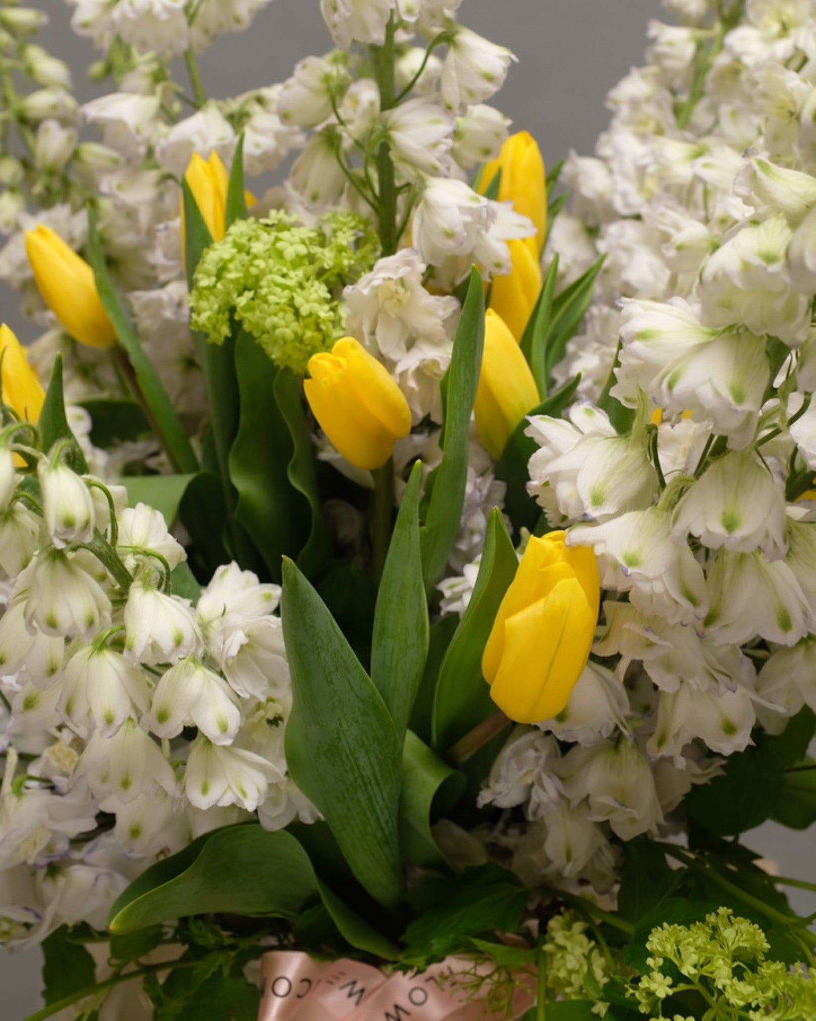 Close-up of green viburnum, soft yellow tulips, and white delphinium – vibrant and textured floral mix