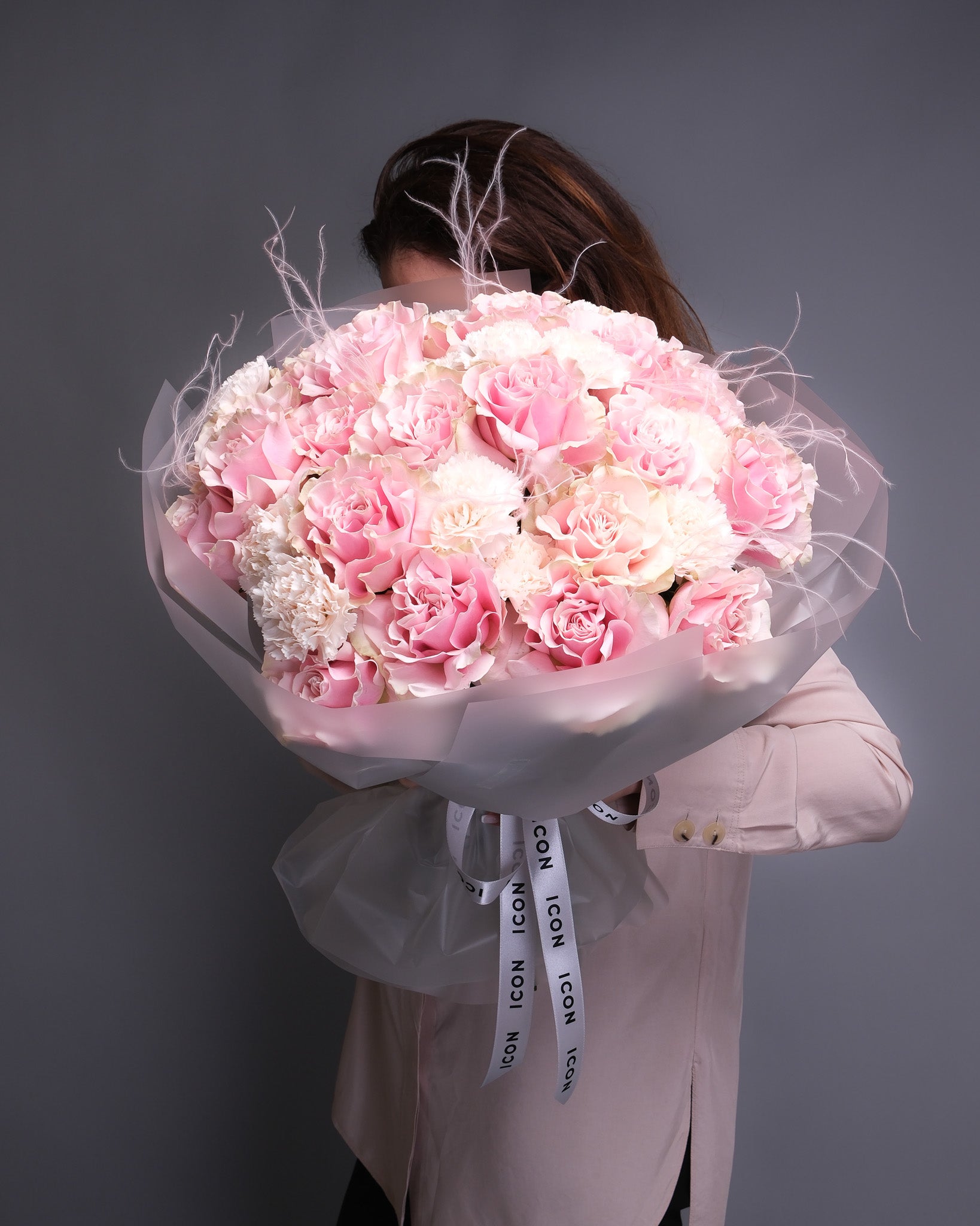 Side-angle view of a handheld bouquet with extra-large pink roses, blush carnations, and stipa grass, showcasing its full, flowing shape and elegant texture.