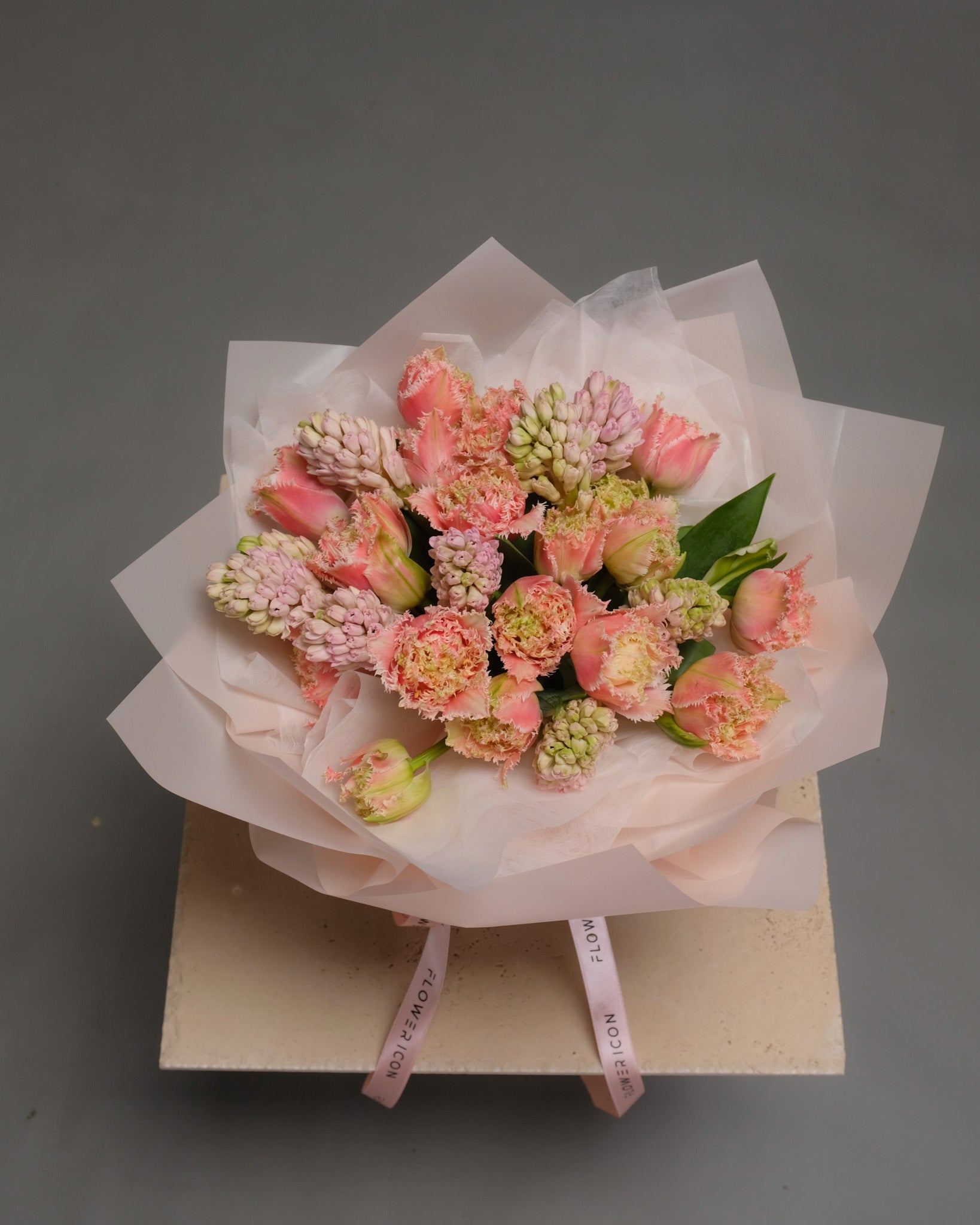 Seasonal bouquet of fluffy tulips and hyacinths in soft pink and orange tones arranged in a glass vase – fresh and modern