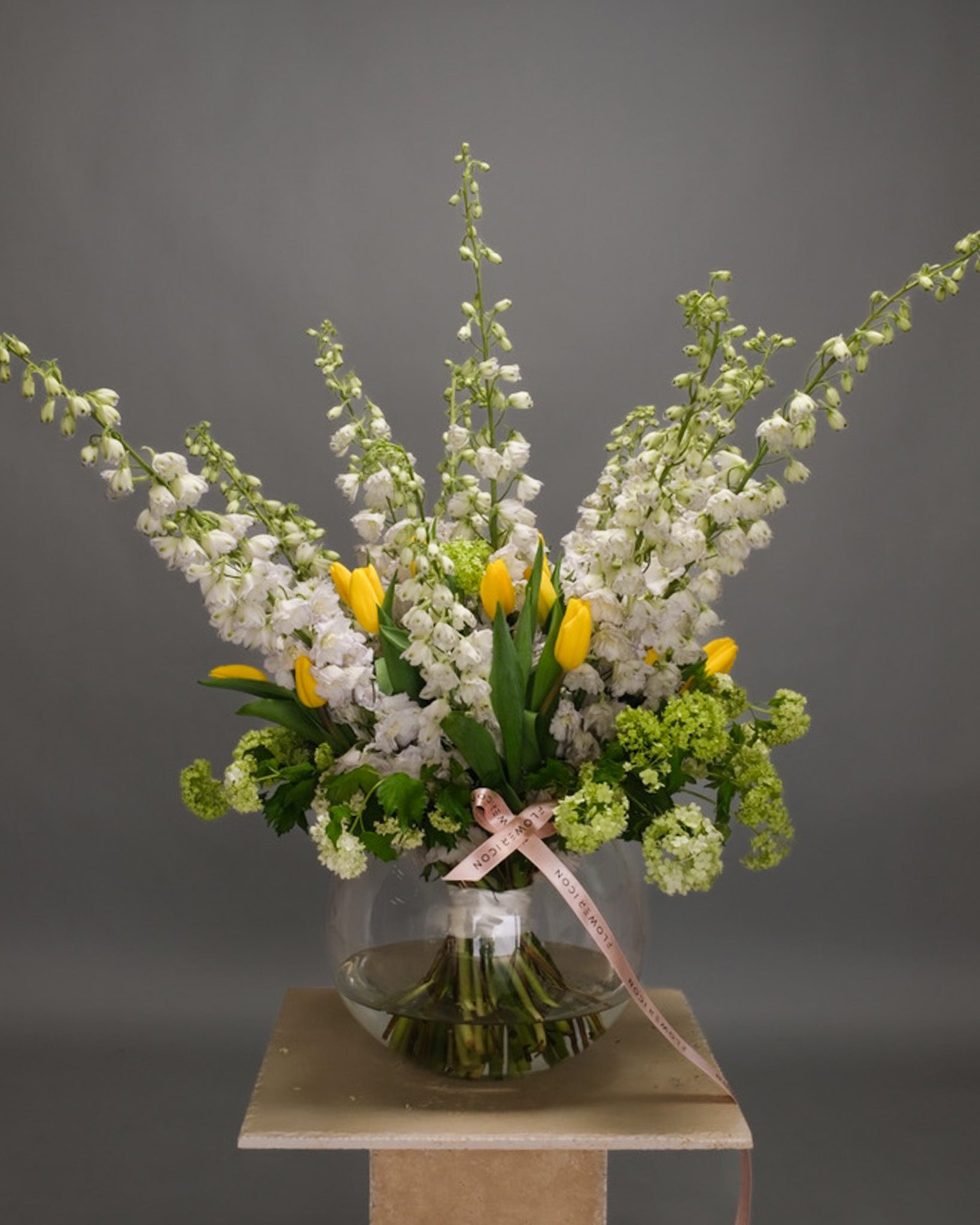 Large spring bouquet in a vase with green viburnum, yellow tulips, and white delphinium – fresh and bright seasonal arrangement