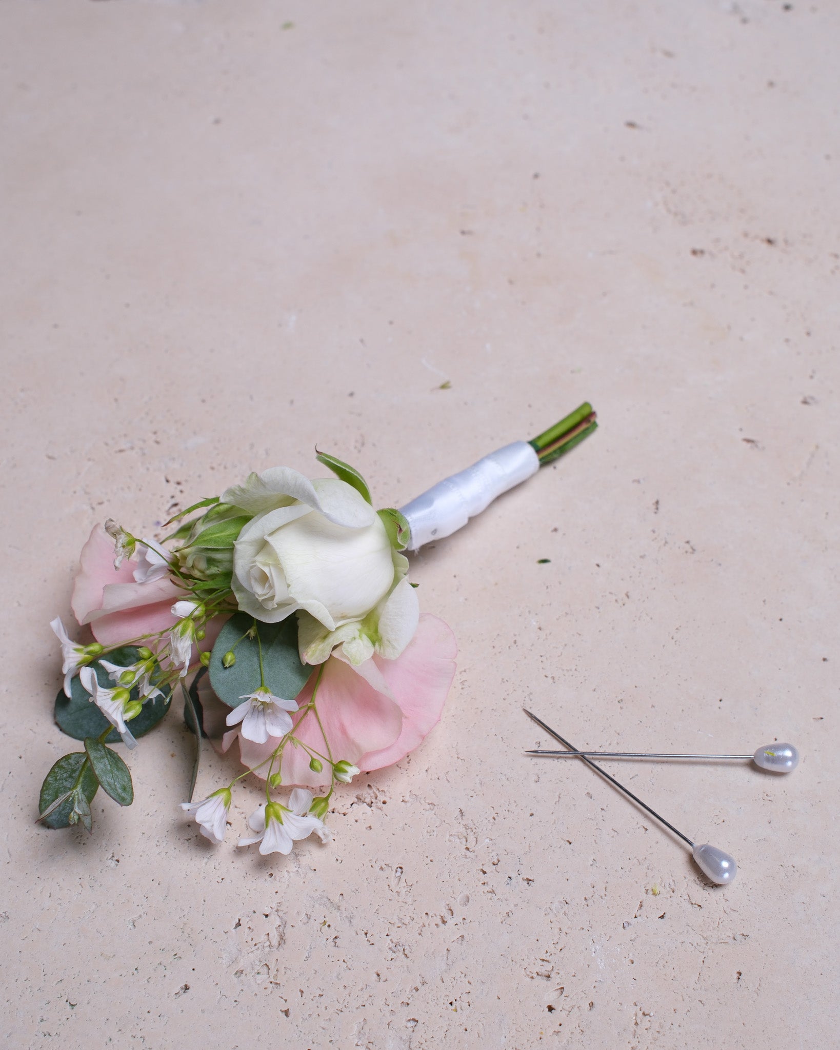 Delicate boutonniere featuring a blush lisianthus bloom, accented with sweet peas and soft greenery for a romantic, refined touch.