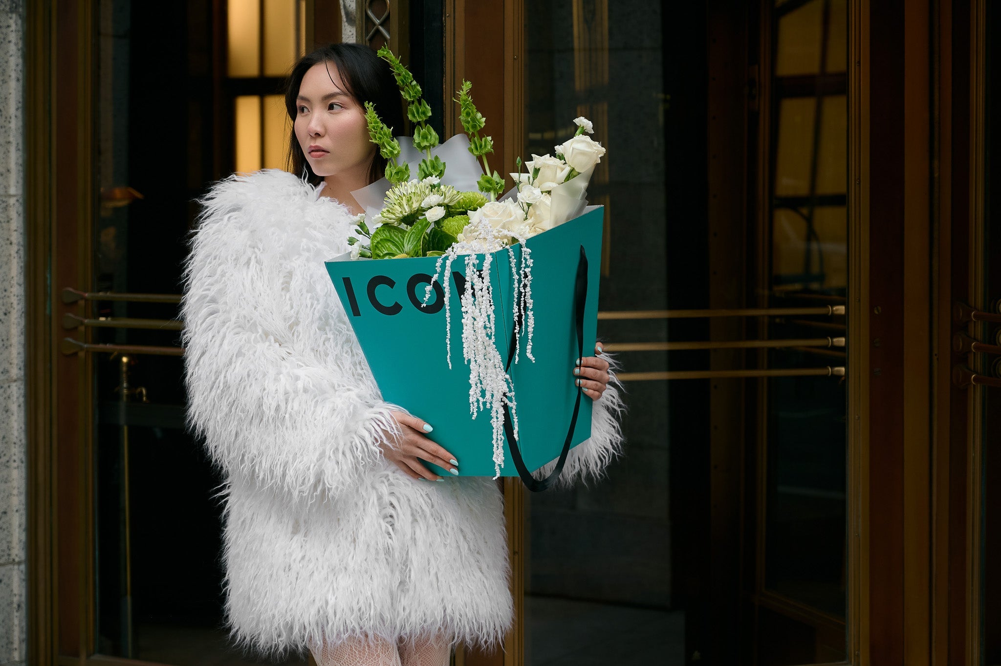 A fashionably dressed woman holding a Flower  Icon Box with green and white flowers