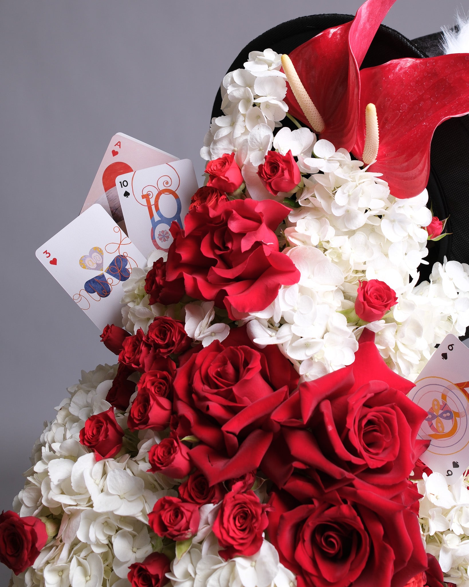 Bouquet of red and white flowers with playing cards, including  cards, on a gray background.