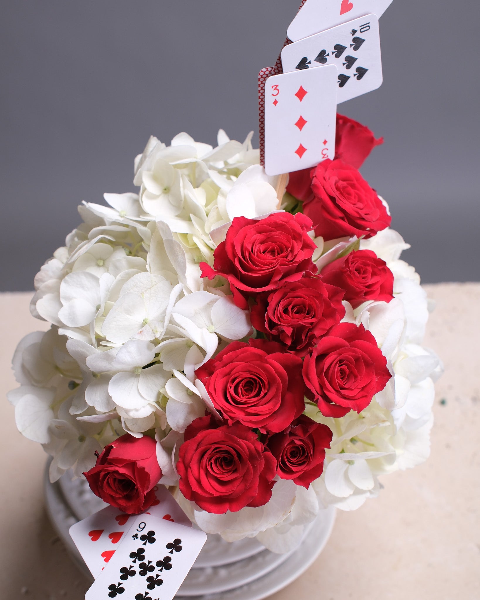 Bouquet of red and white flowers with playing cards on a gray background