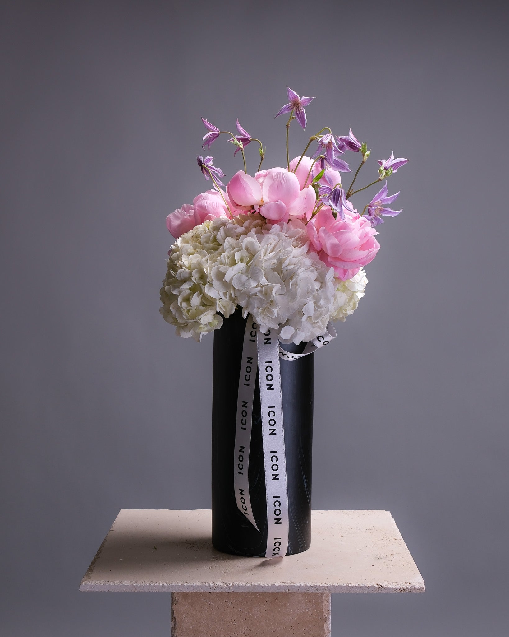 Floral arrangement in a black vase with 'ICON' branding on a gray background