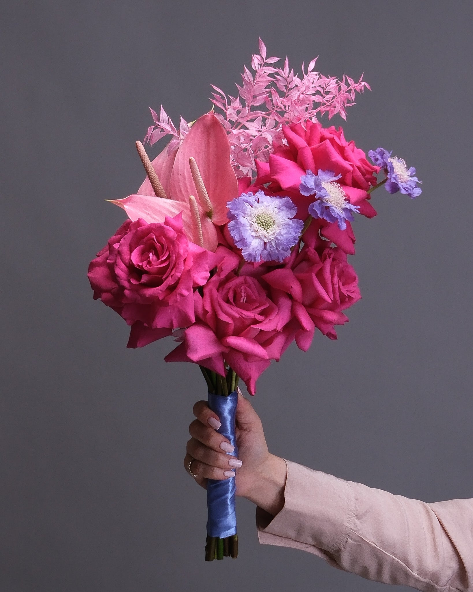 Pink Bridal Bouquet of pink flowers held by a hand against a gray background