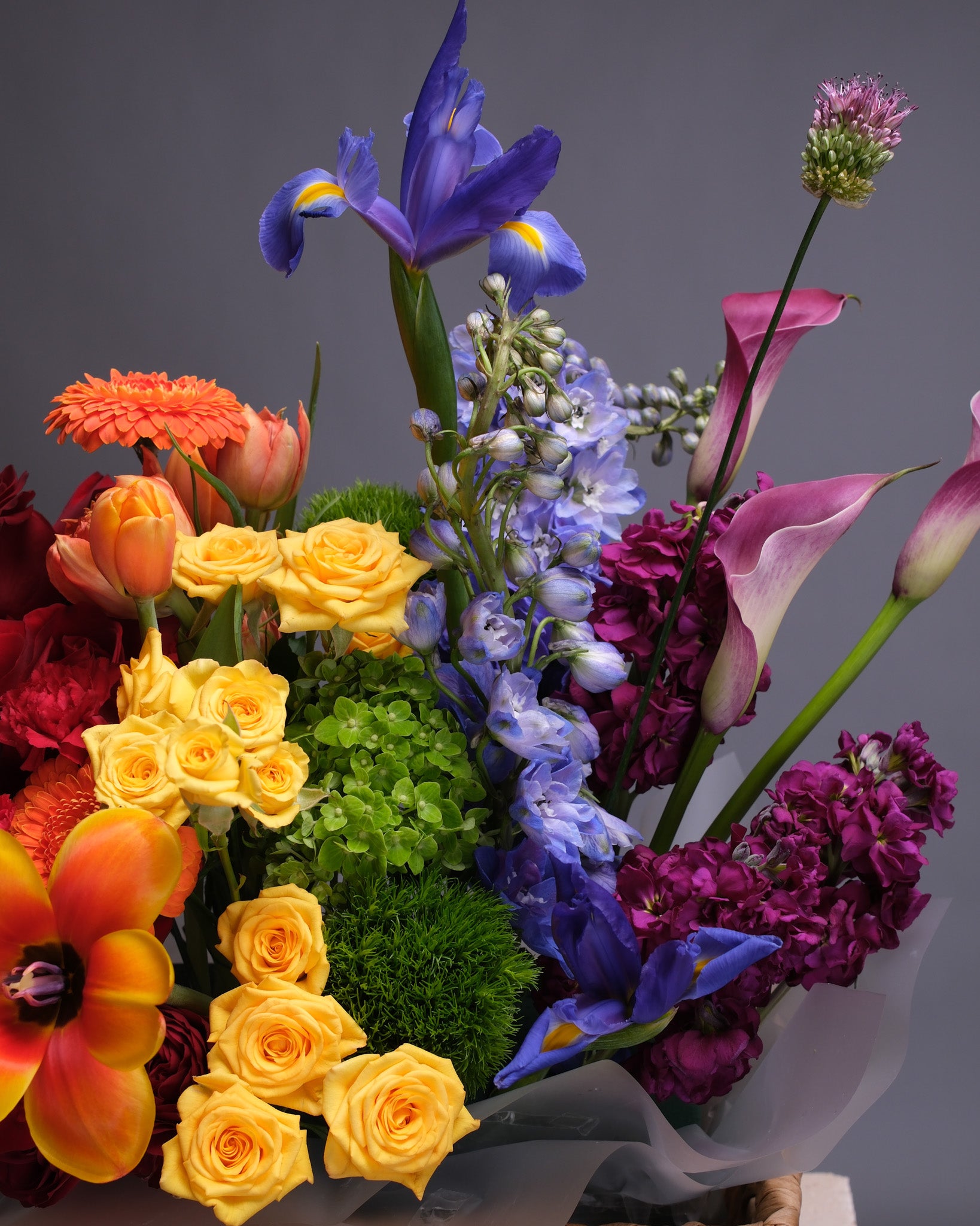 Close-up of the rainbow floral basket showing detailed textures of colorful flowers like calla lilies, delphinium, and roses.