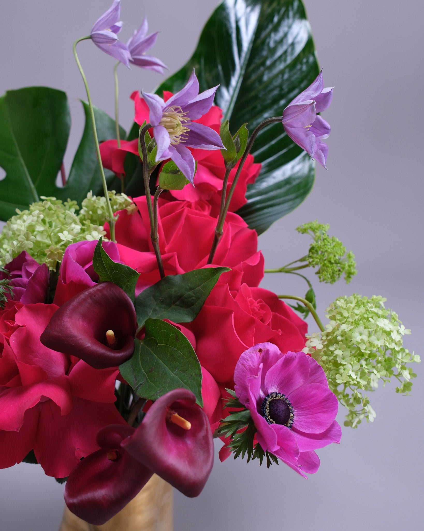 Bouquet of flowers including red roses, purple callas, and green hydrangeas on a gray background