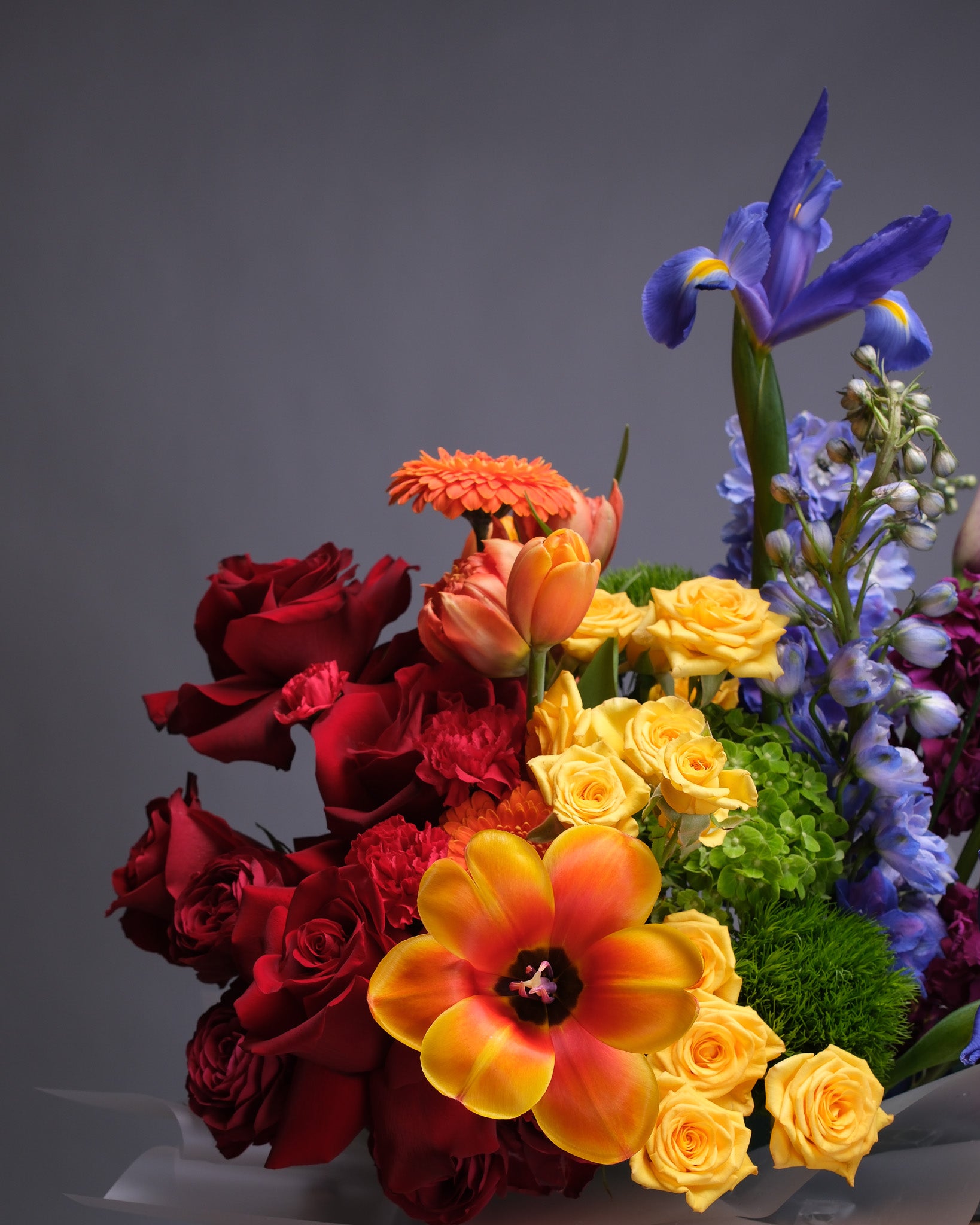Detailed view highlighting the rich mix of rainbow-colored flowers arranged tightly in a basket with lush greenery.
