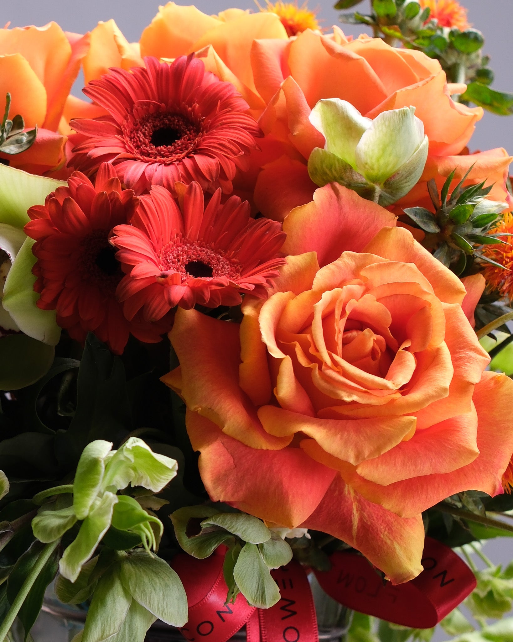 Bouquet of flowers including red gerberas and orange roses with a visible ribbon.