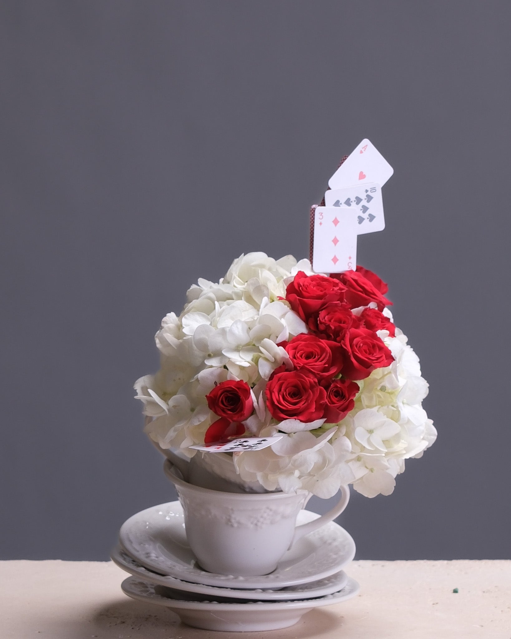 Floral arrangement with red and white flowers in a white teacup on a gray background