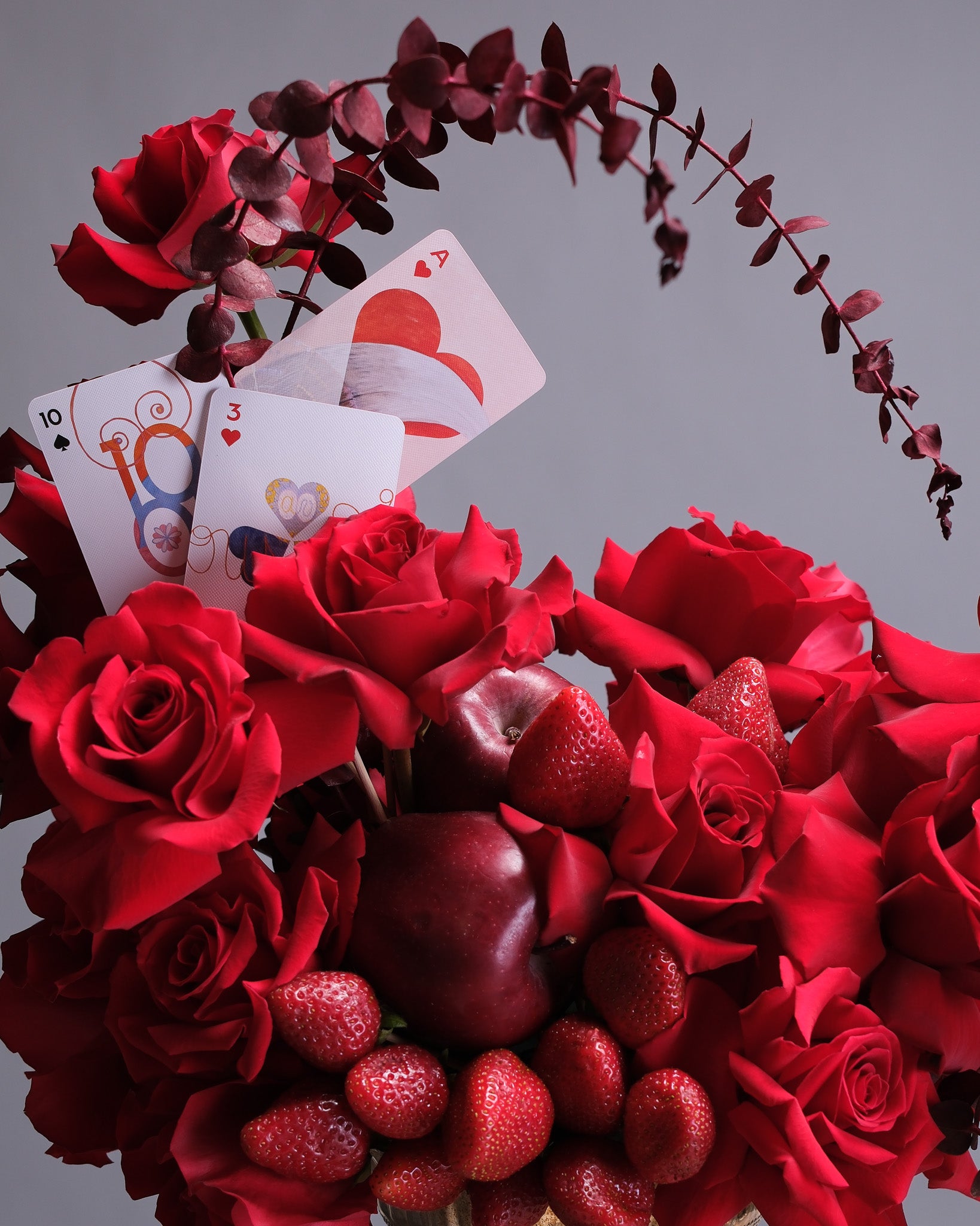 Bouquet of red roses with strawberries and playing cards on a gray background