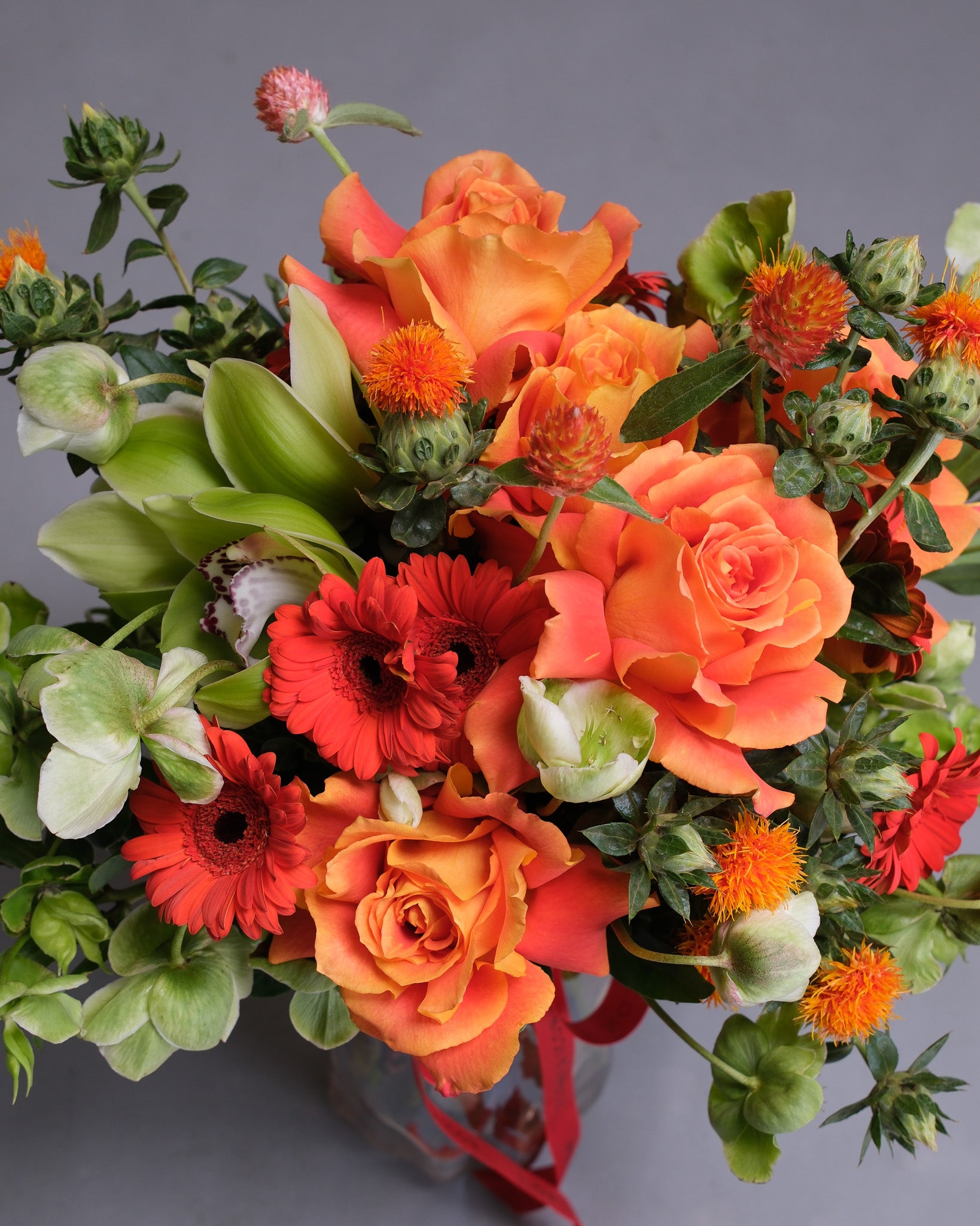 Bouquet of orange, red, and green flowers with greenery on a gray background