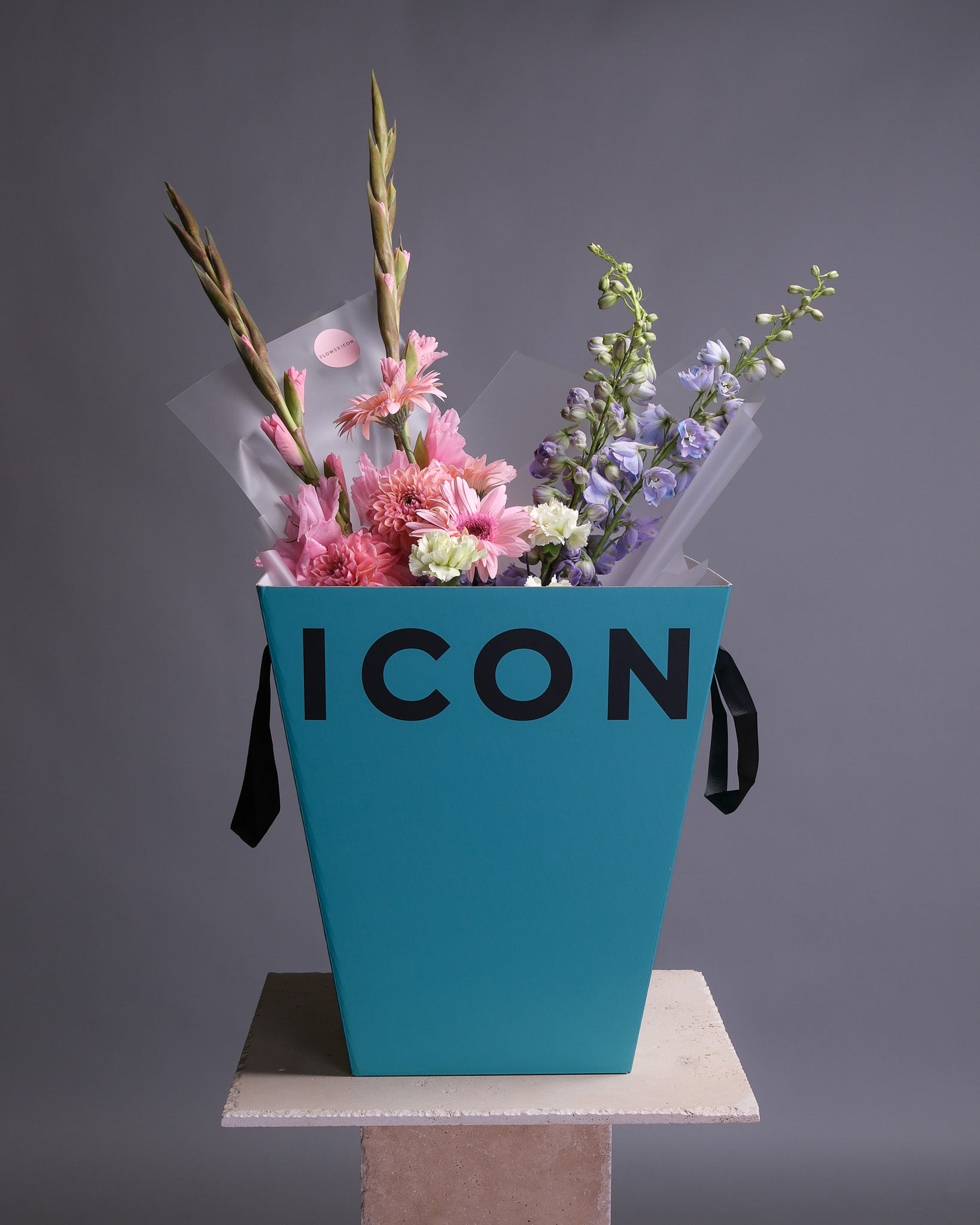 Floral arrangement in a blue box with 'ICON' branding on a gray background