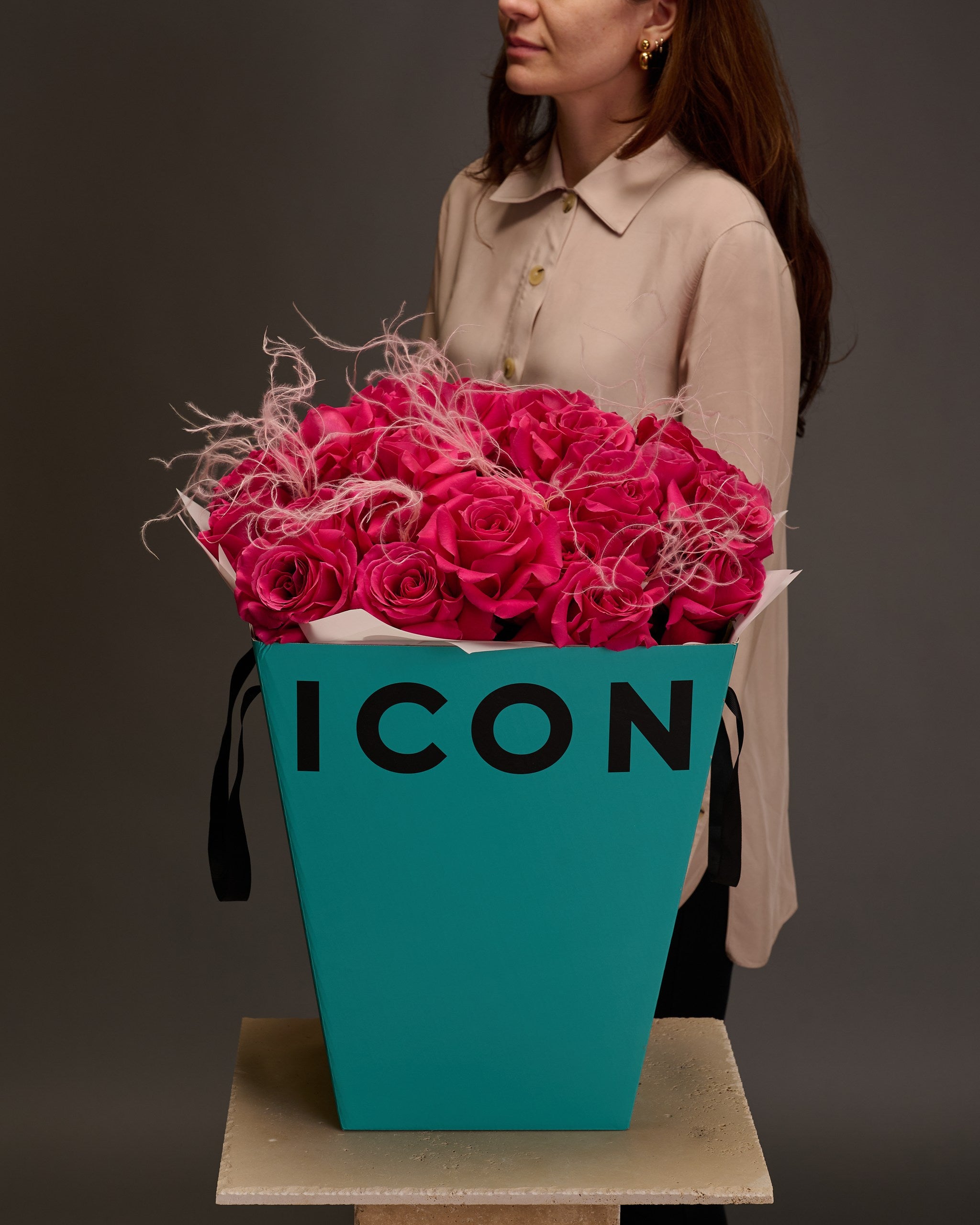 Woman standing behind a luxury bouquet of hot pink roses and stipa in Flower Icon gift box