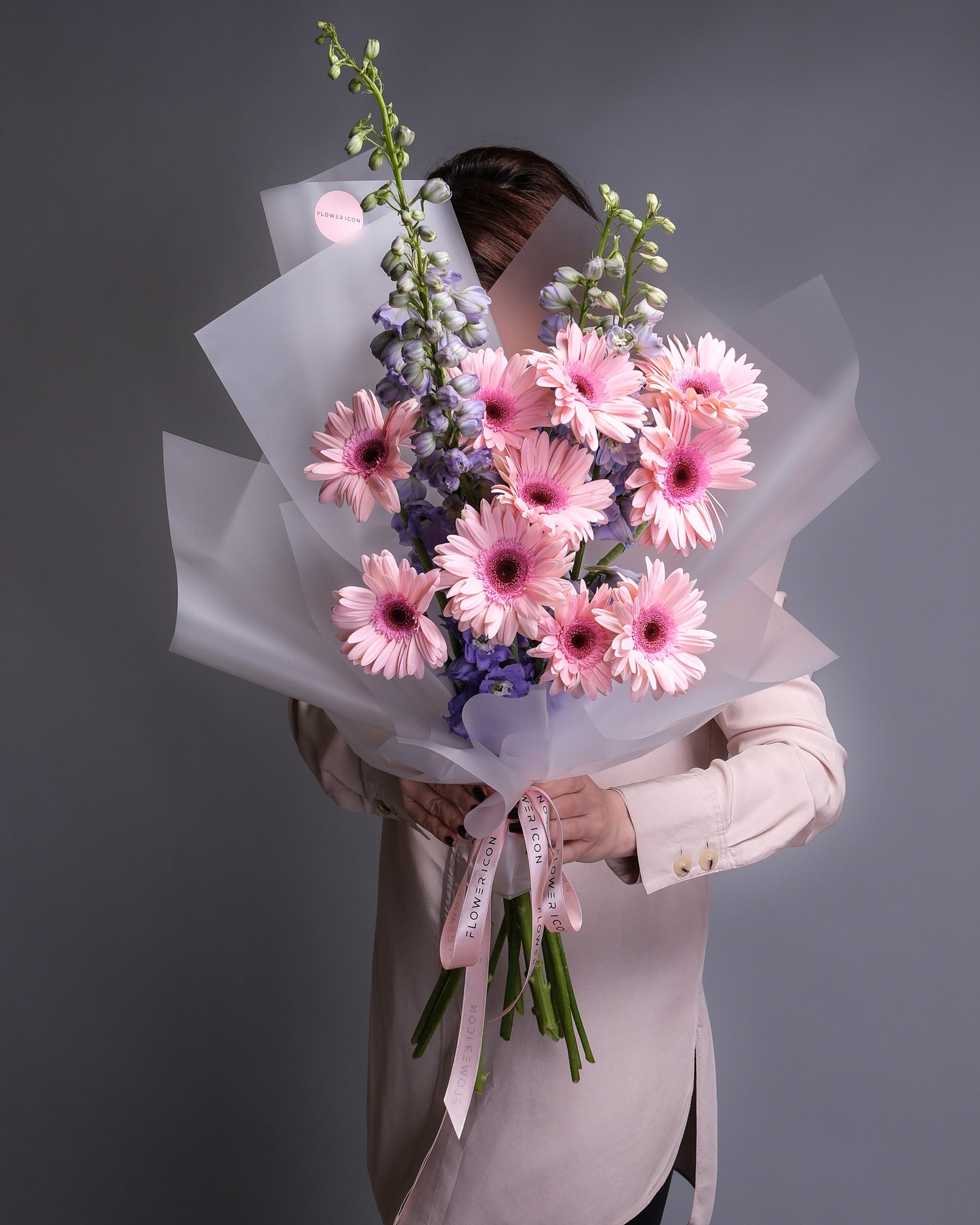 Person holding a bouquet of pink flowers against a gray background