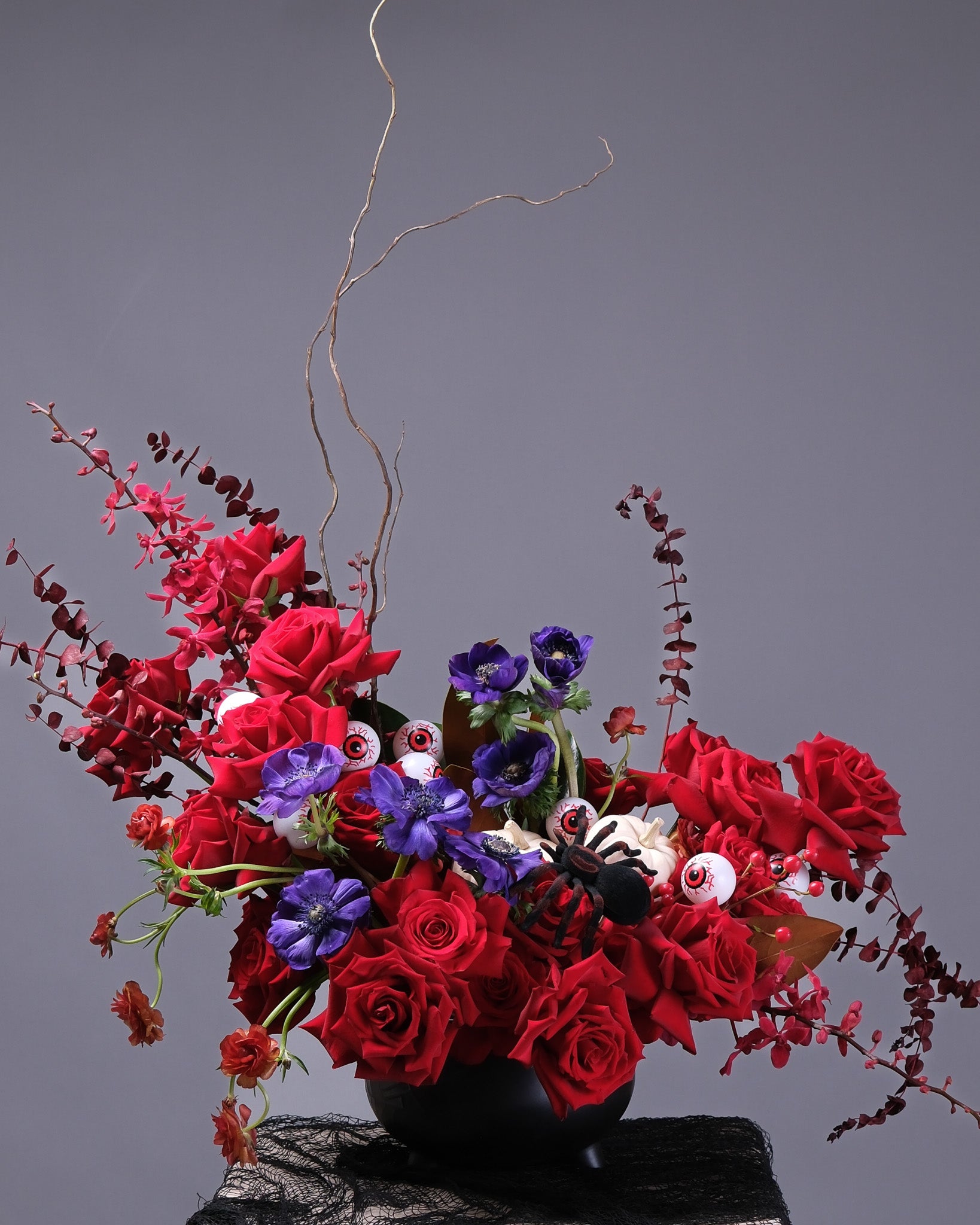 Bouquet of red and purple flowers in a black kettle on a gray background. Halloween arrangement. 