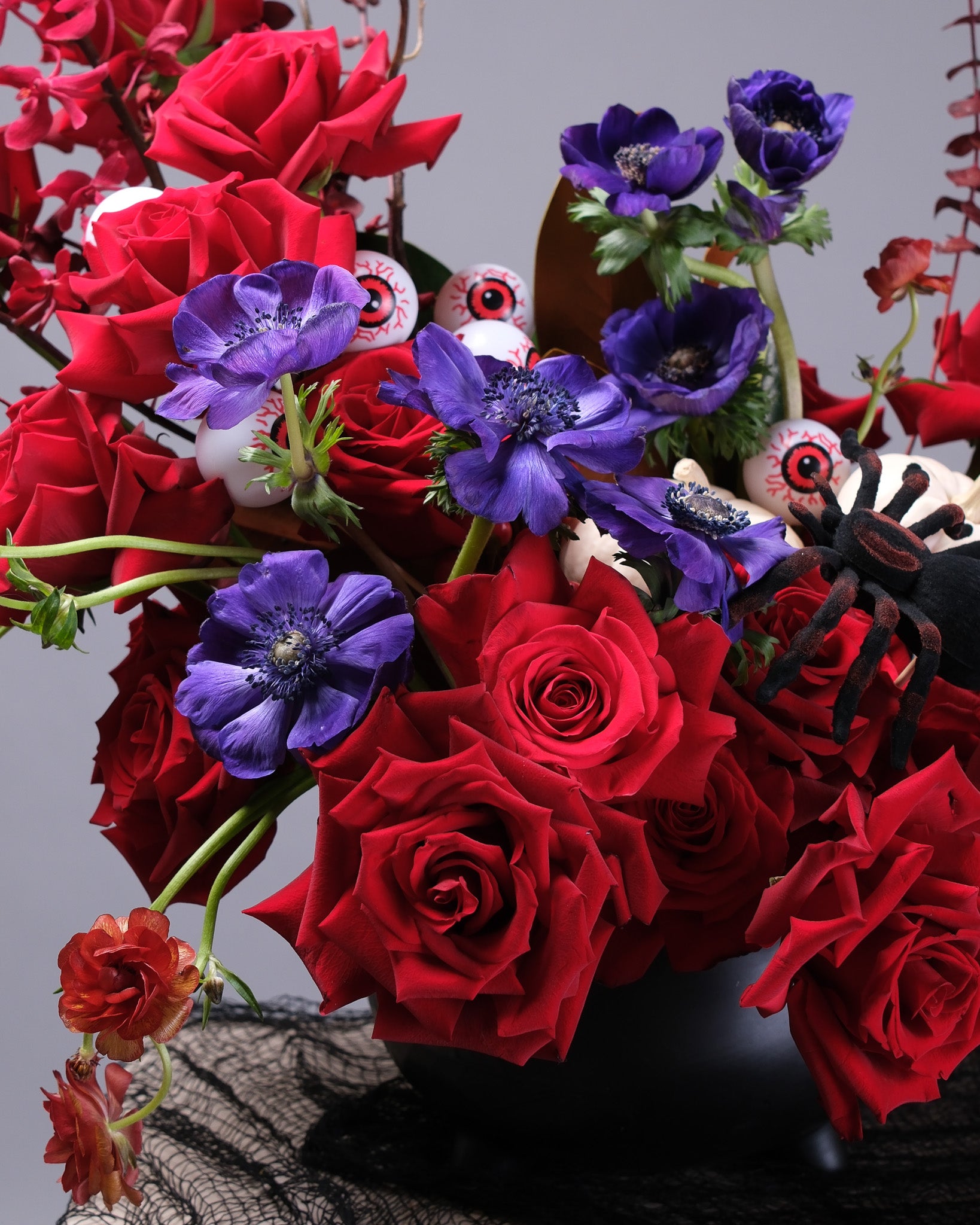 Halloween arrangement of red roses and purple flowers on a textured surface with a neutral background