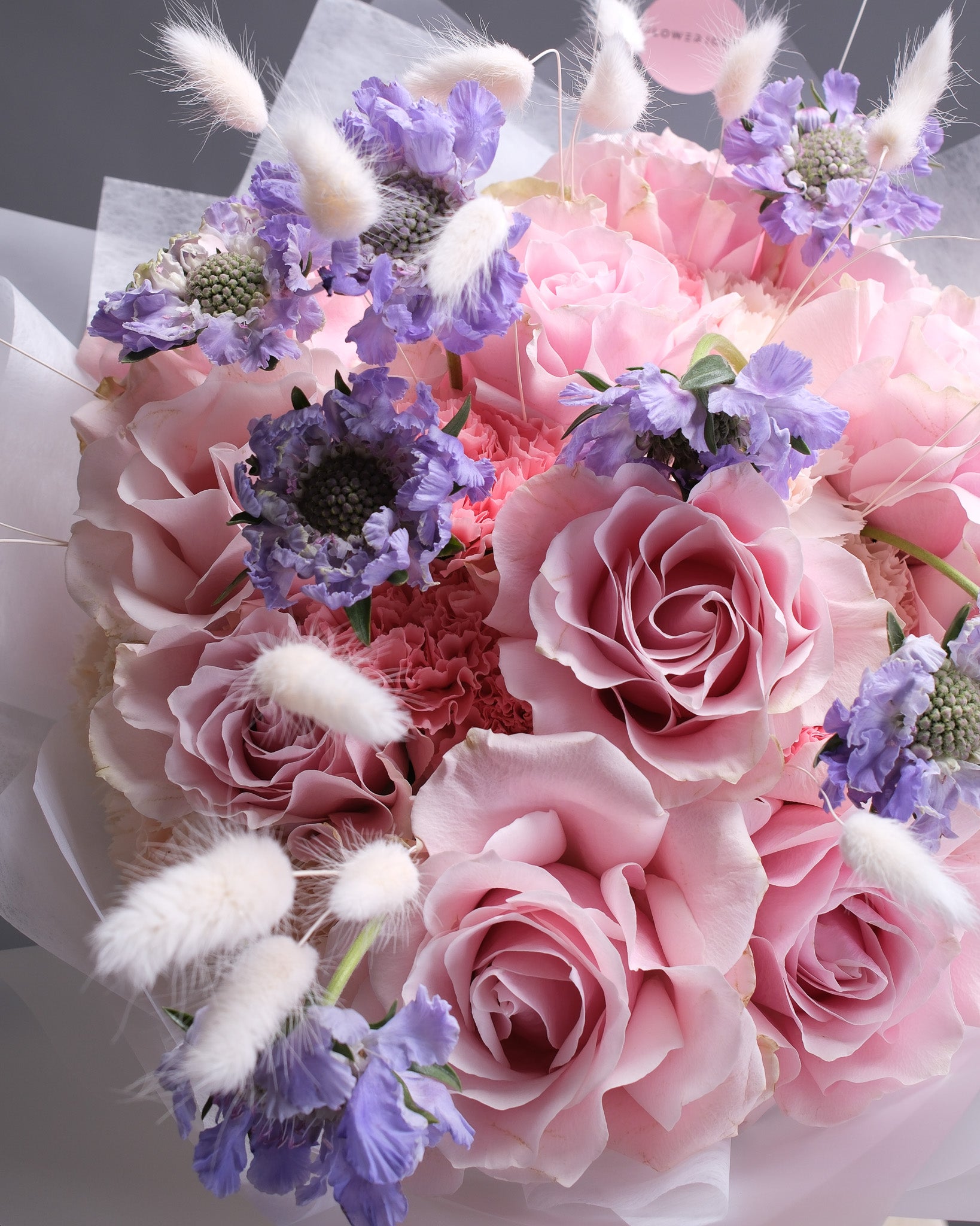 Bouquet of pink and purple flowers with white fluffy elements on a gray background