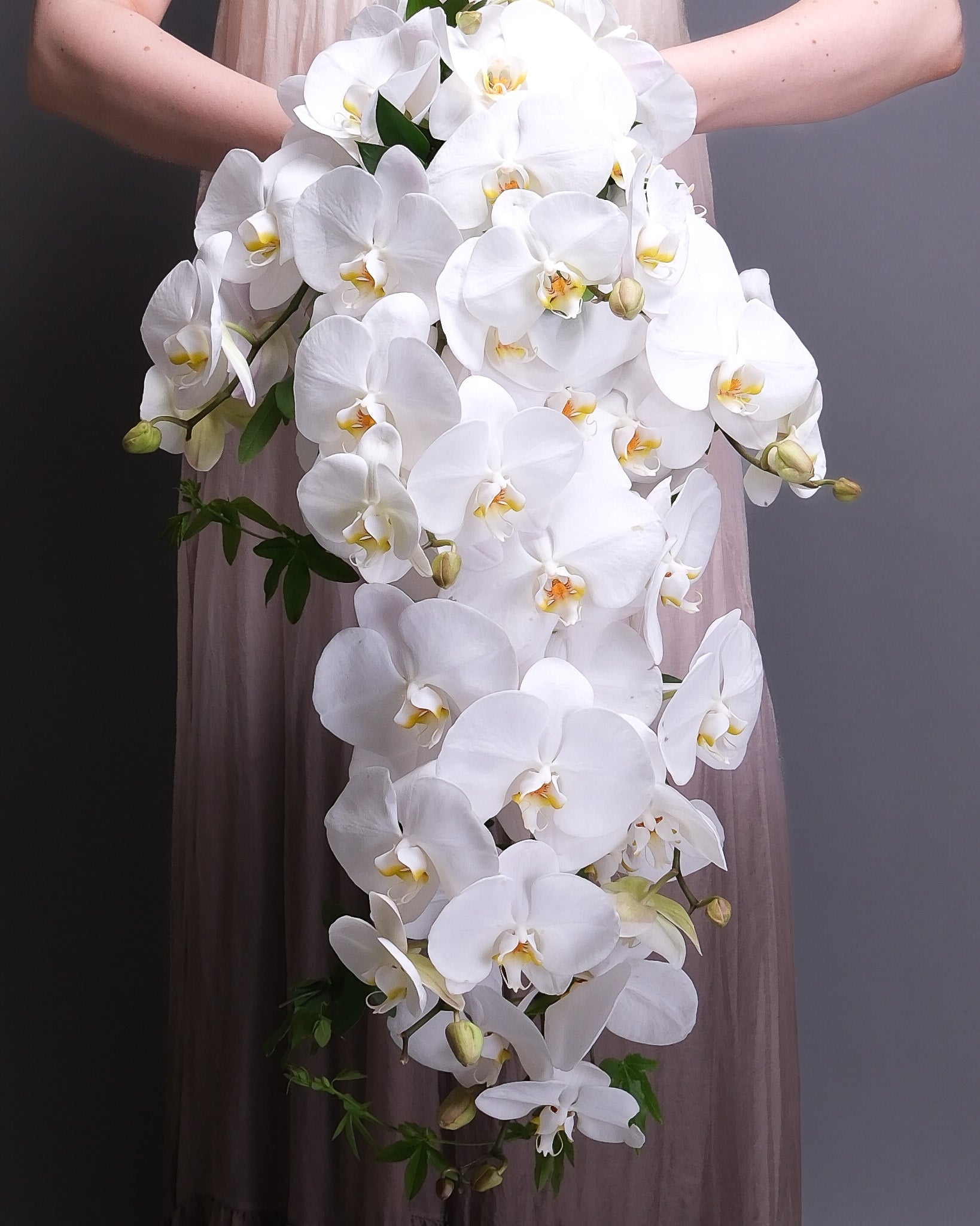 Bouquet of white orchids held by a person against a neutral background