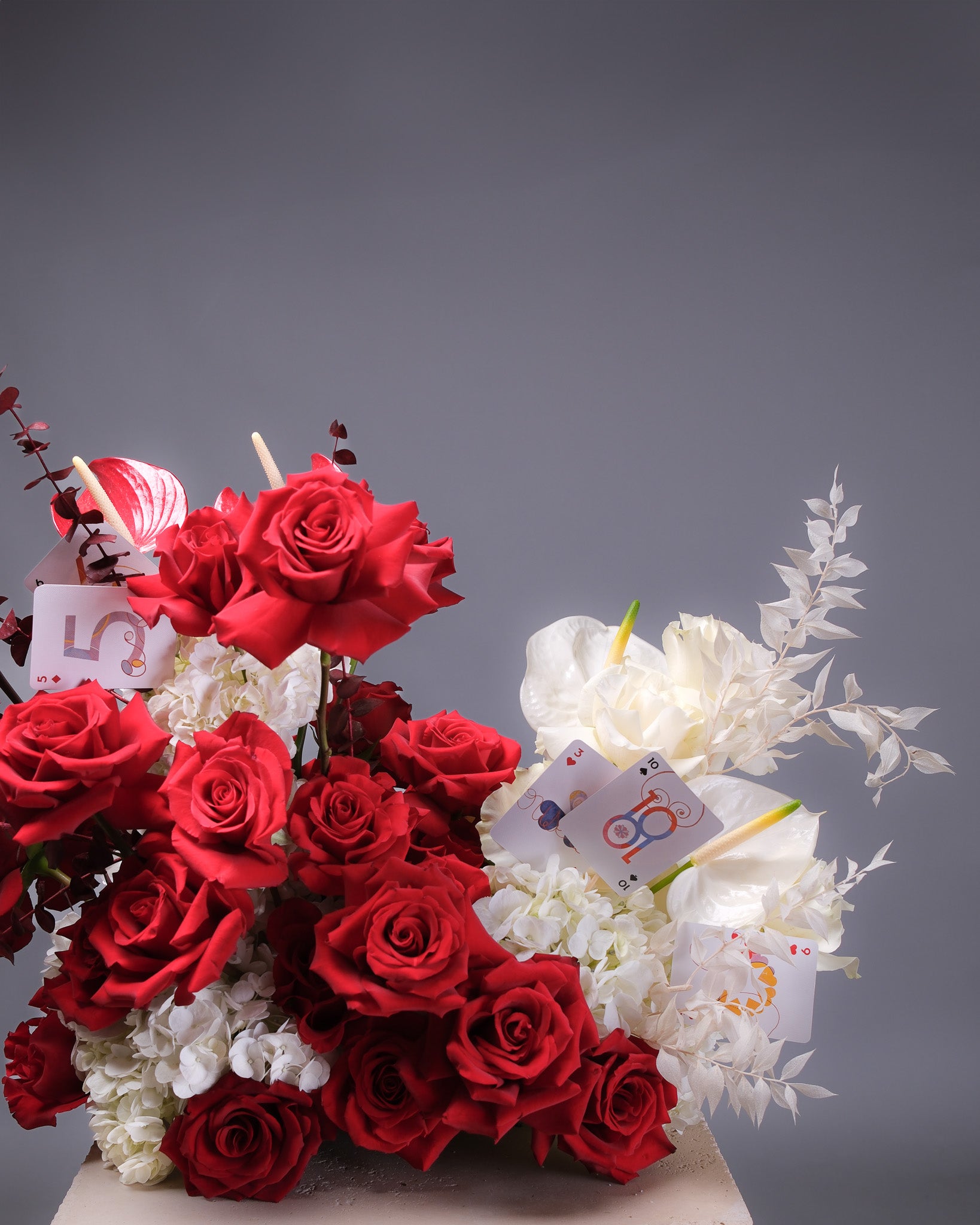 Bouquet of red and white flowers with playing card elements on a gray background