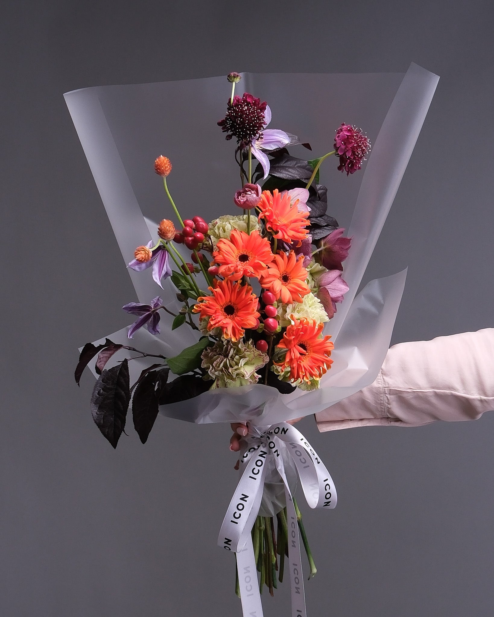 Bouquet of orange and burgundy flowers with a Flower Icon ribbon against a dark background