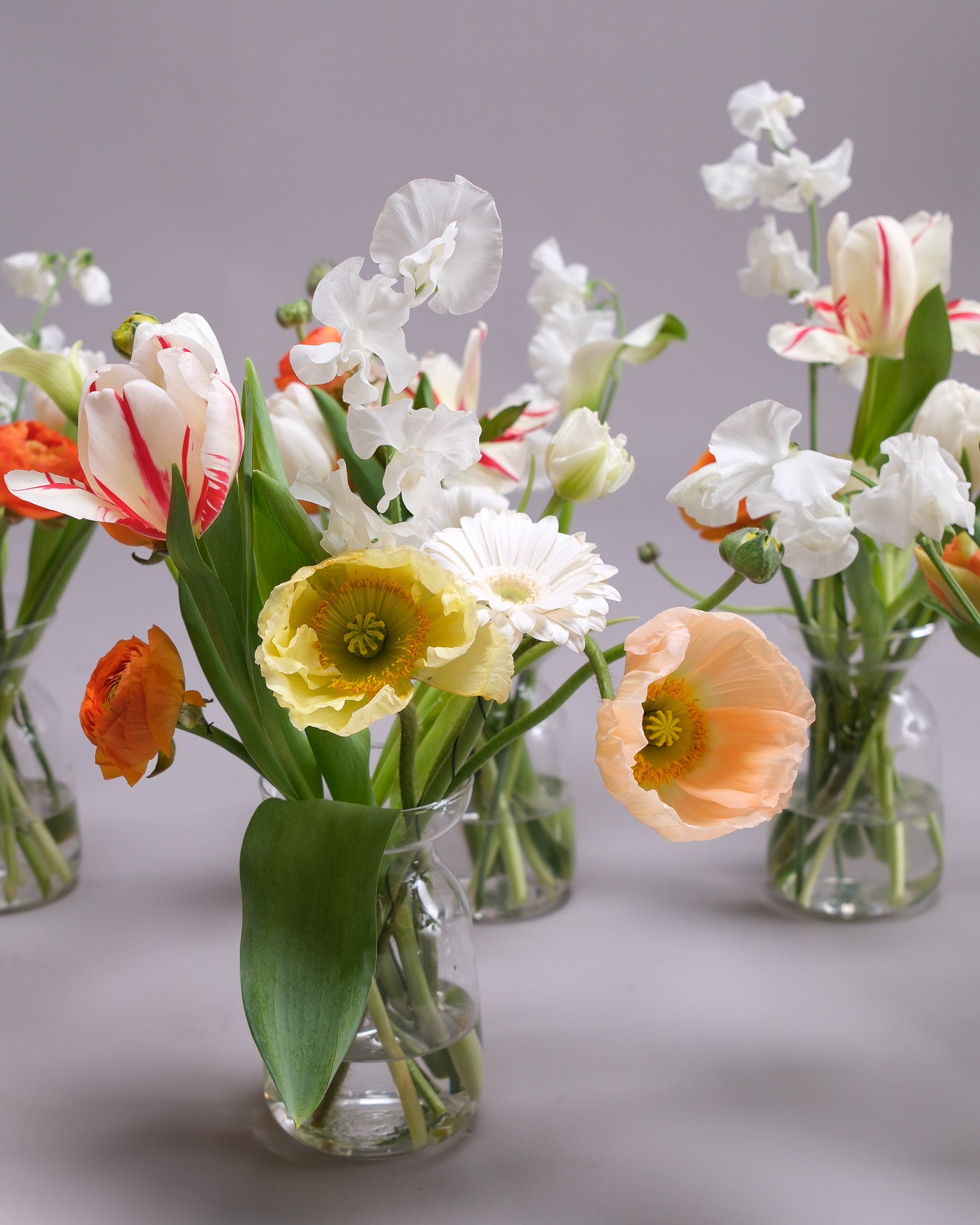 Clear glass vases with assorted flowers on a gray background