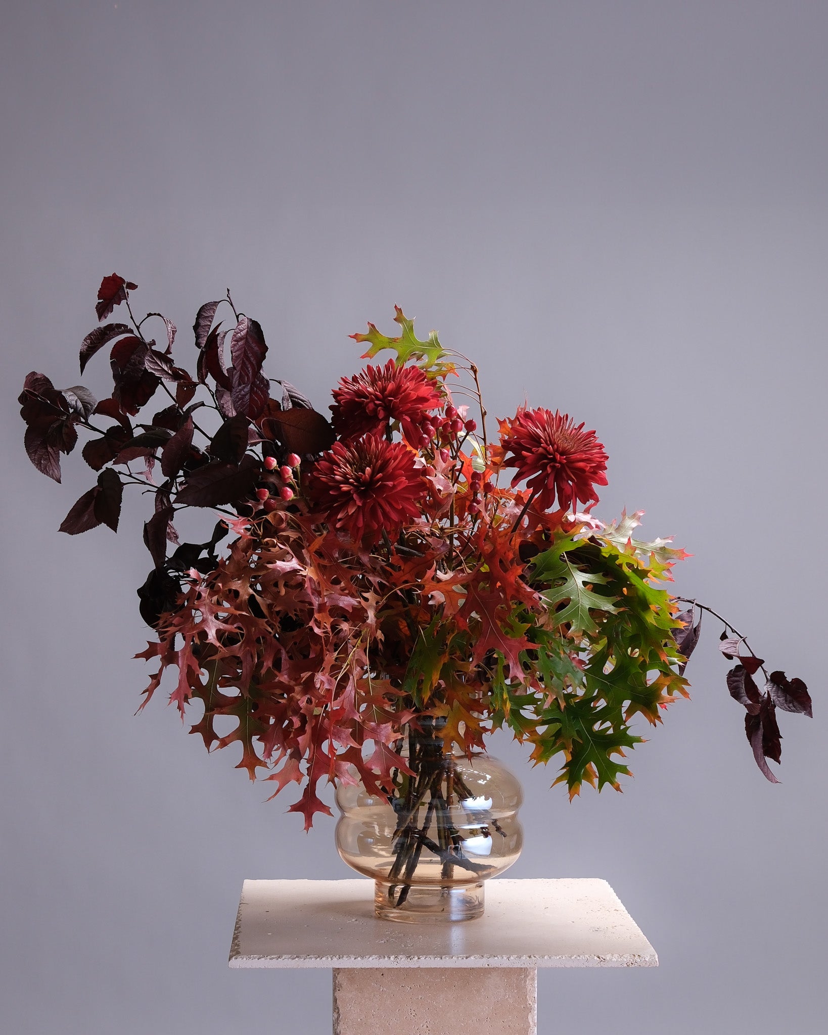 Bouquet of red and green flowers in a clear vase on a gray background
