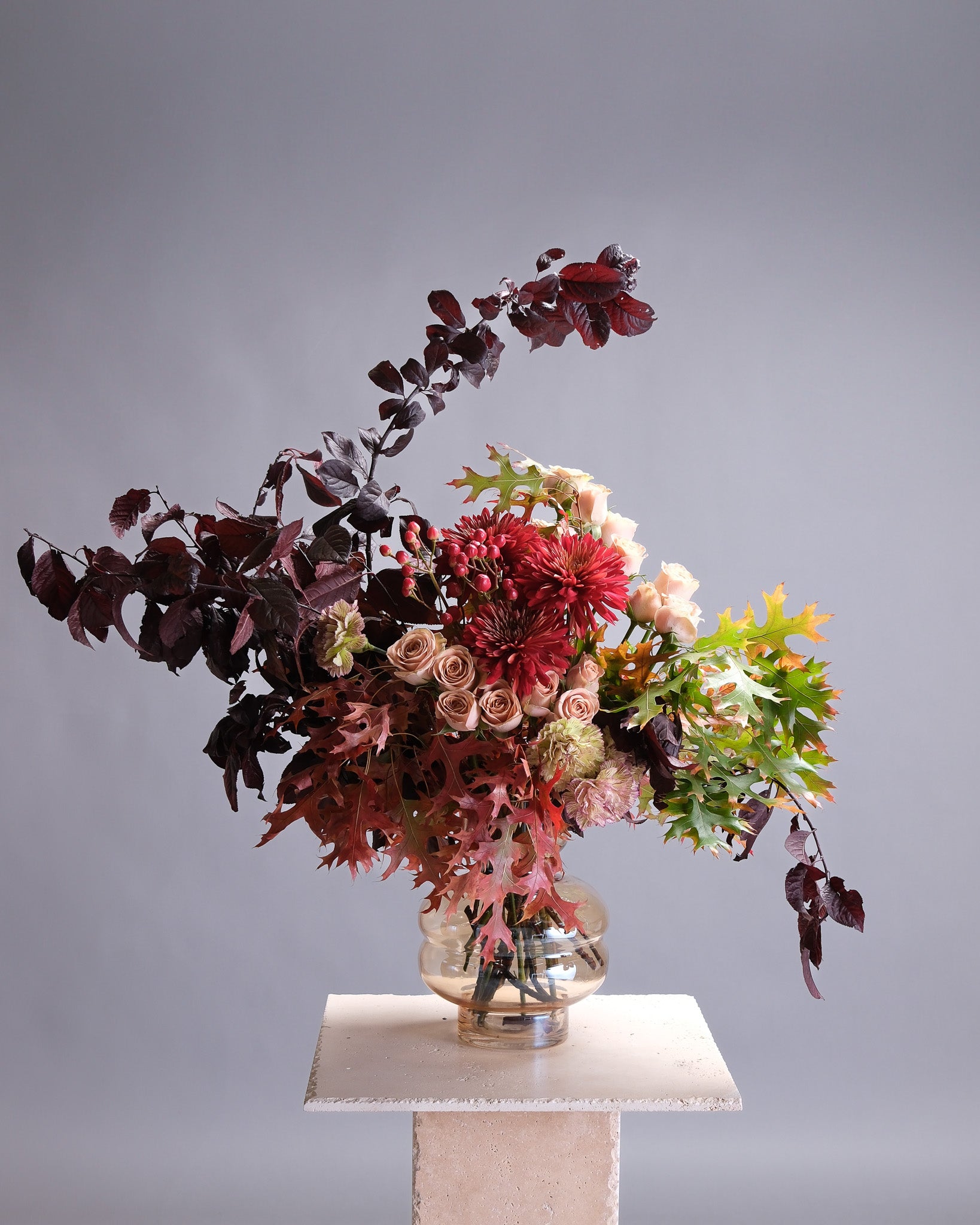 Colorful floral arrangement on a pedestal against a gray background