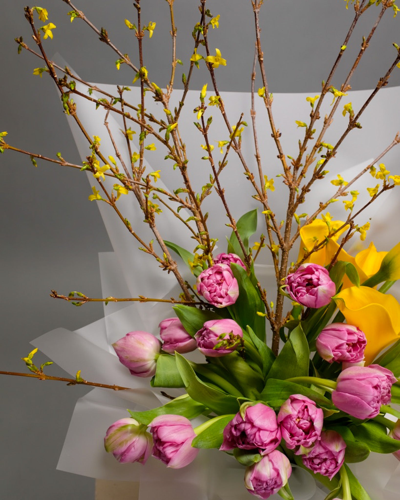 Close-up of purple tulips and yellow calla lilies with forsythia – vibrant seasonal mix with bold color contrast